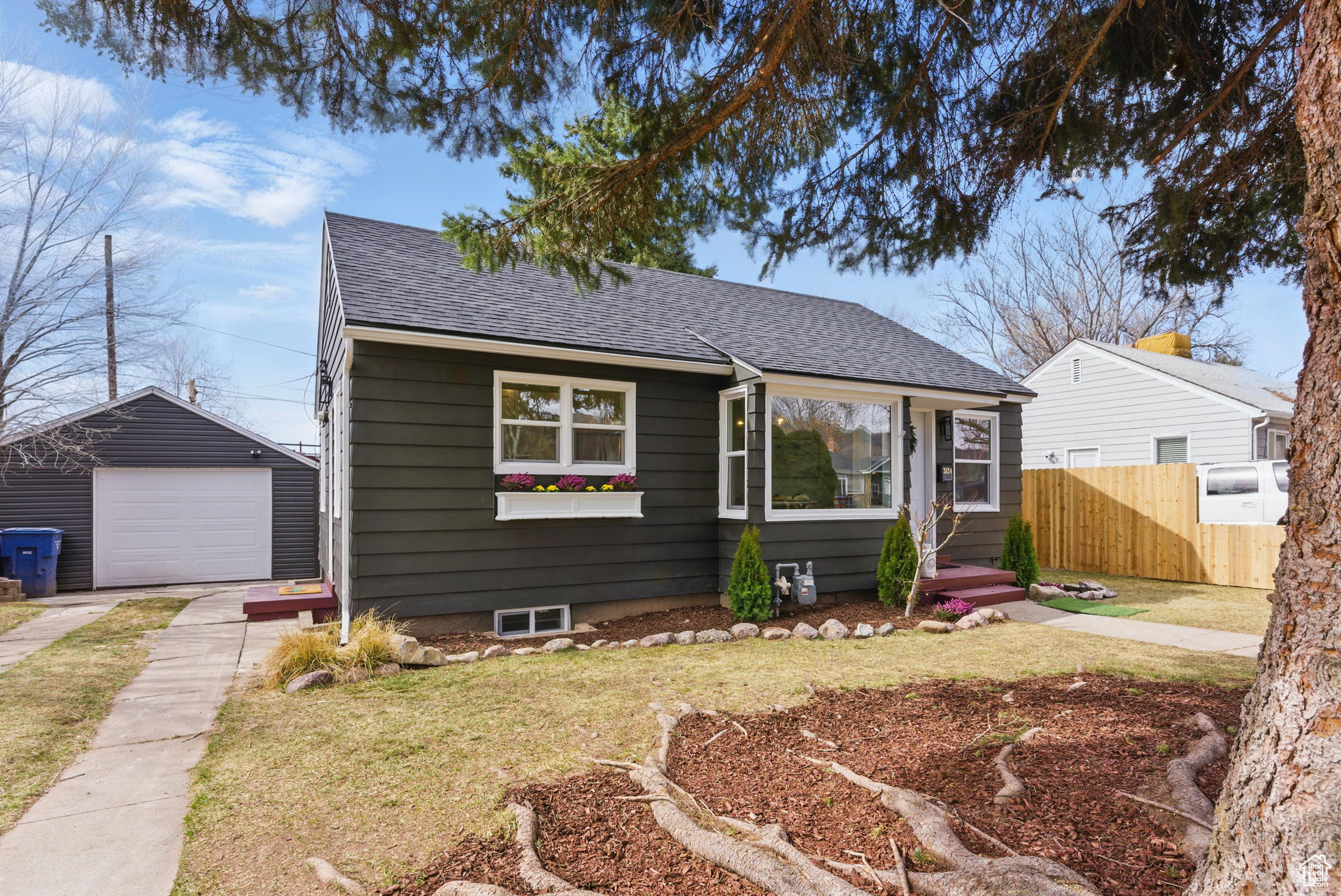 Bungalow-style home with an outbuilding, fence, a shingled roof, concrete driveway, and a garage