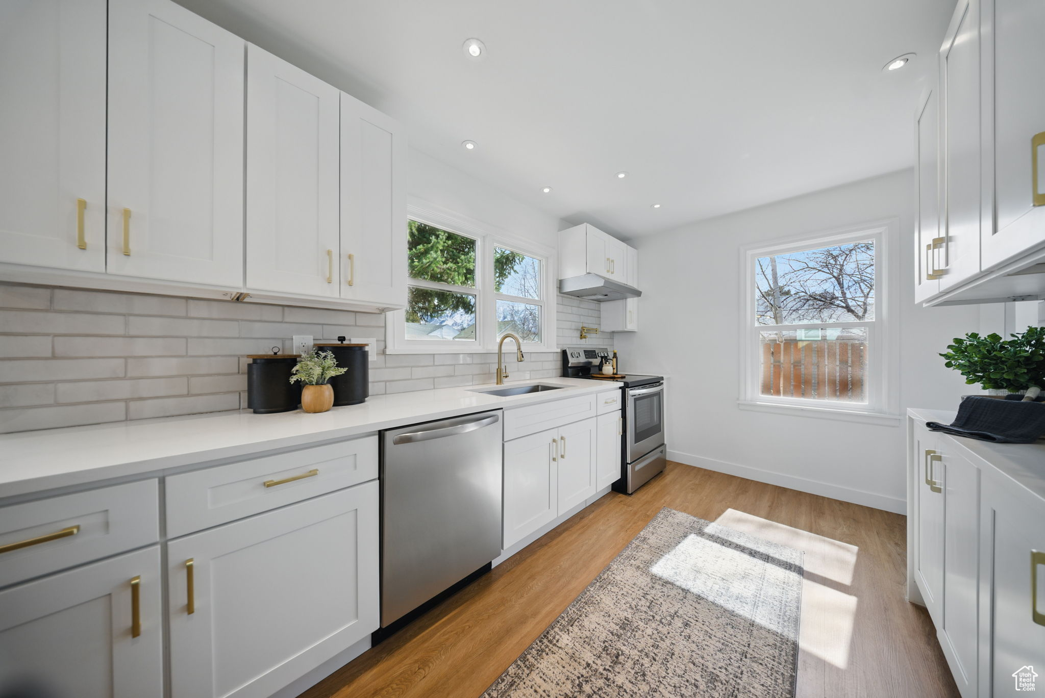 Kitchen featuring light wood-style flooring, a sink, decorative backsplash, under cabinet range hood, and appliances with stainless steel finishes