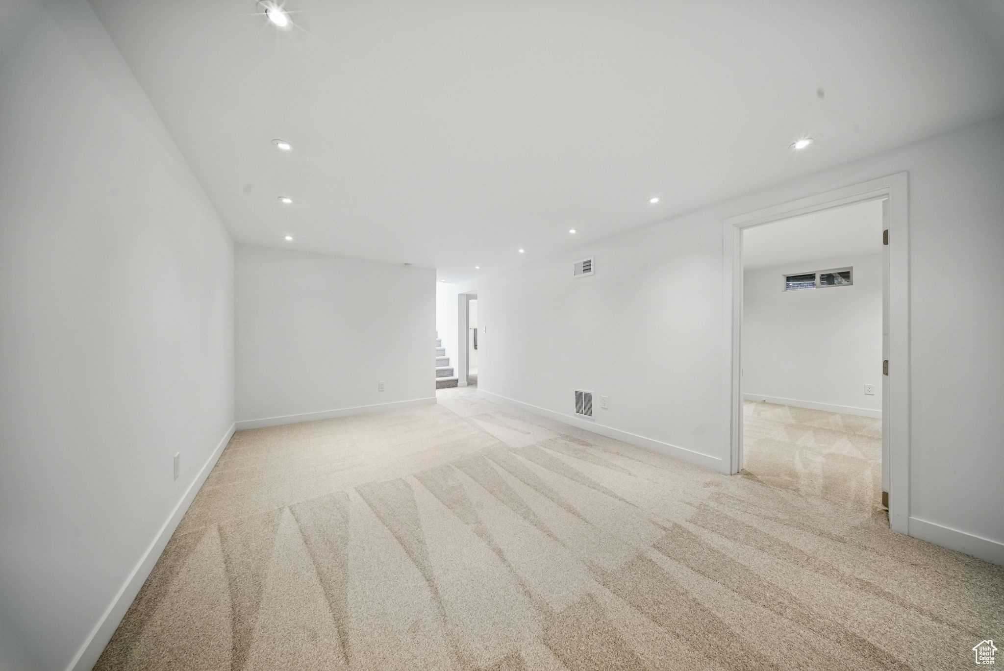Empty room with visible vents, light carpet, recessed lighting, stairway, and baseboards