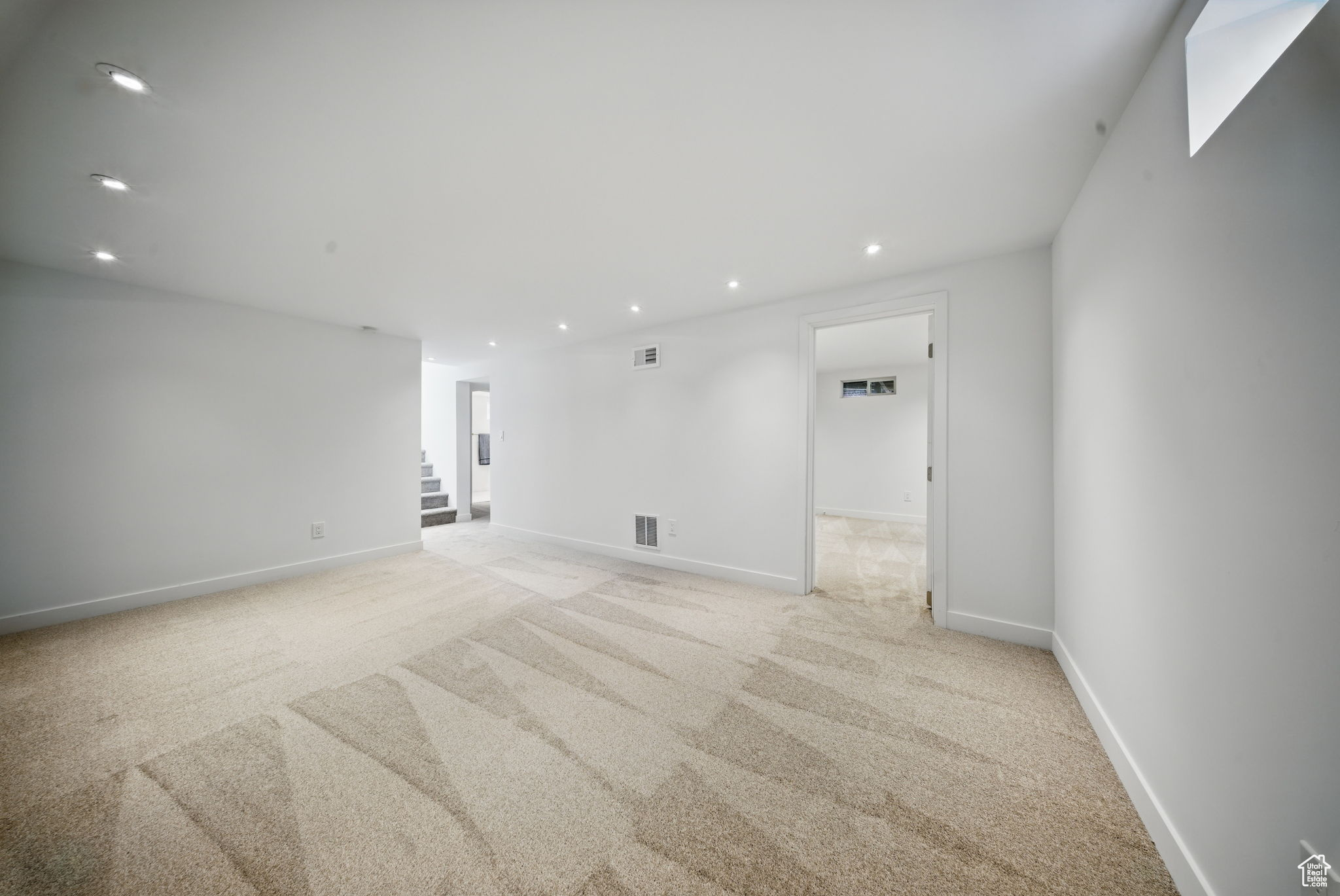 Empty room featuring stairs, recessed lighting, visible vents, and light carpet