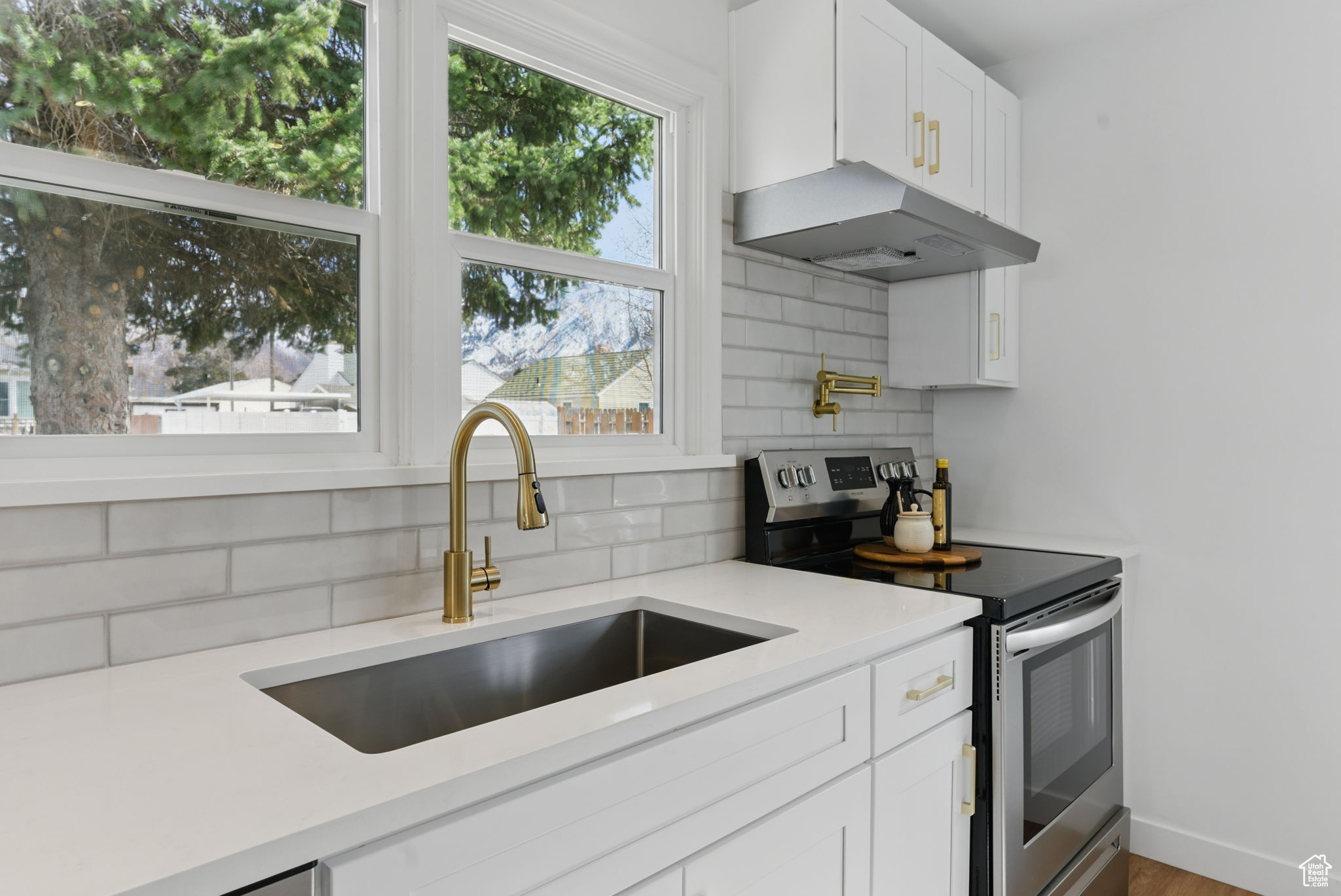 Kitchen featuring backsplash, under cabinet range hood, stainless steel electric stove, light countertops, and a sink