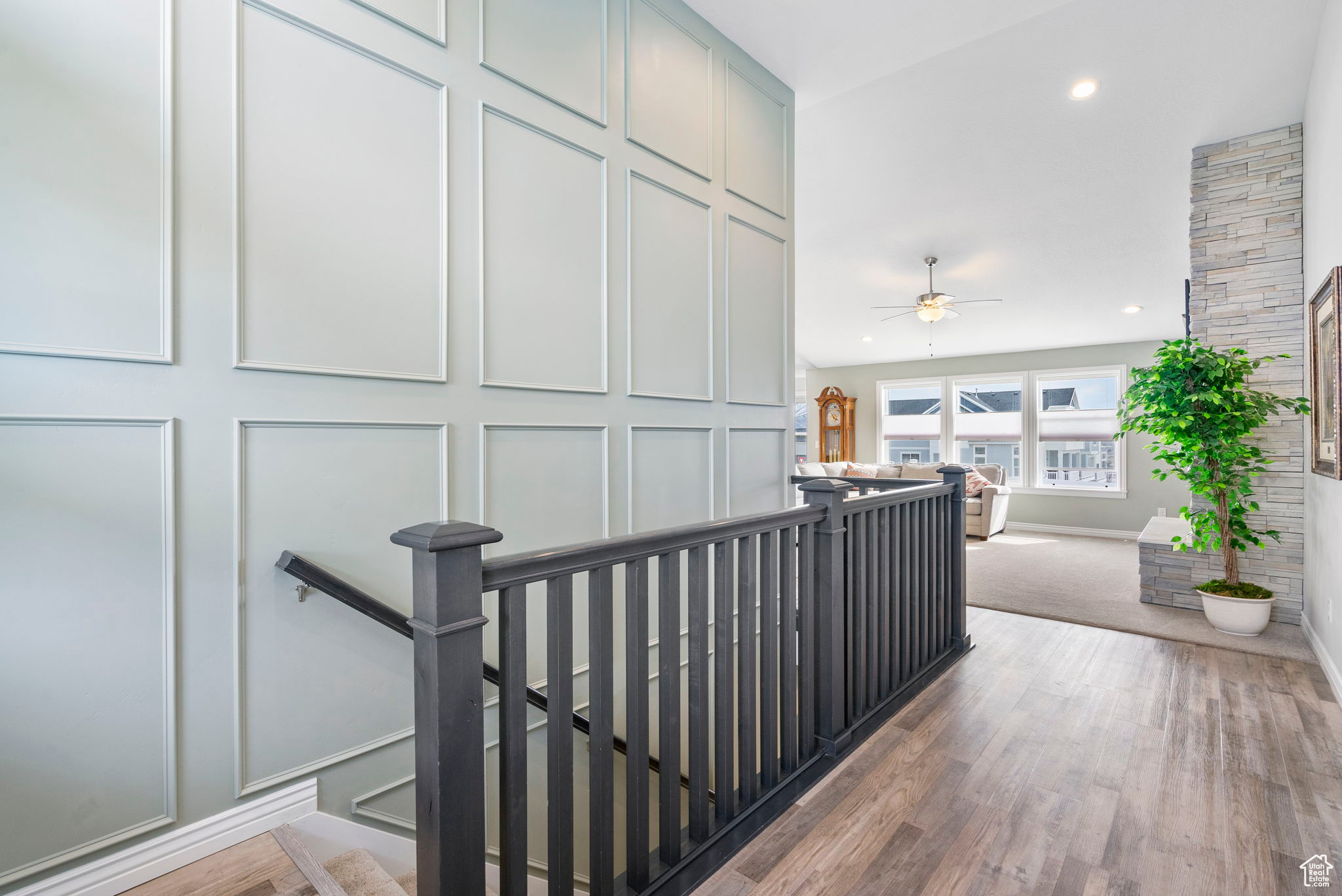 Hall with an upstairs landing, a decorative wall, recessed lighting, and wood finished floors