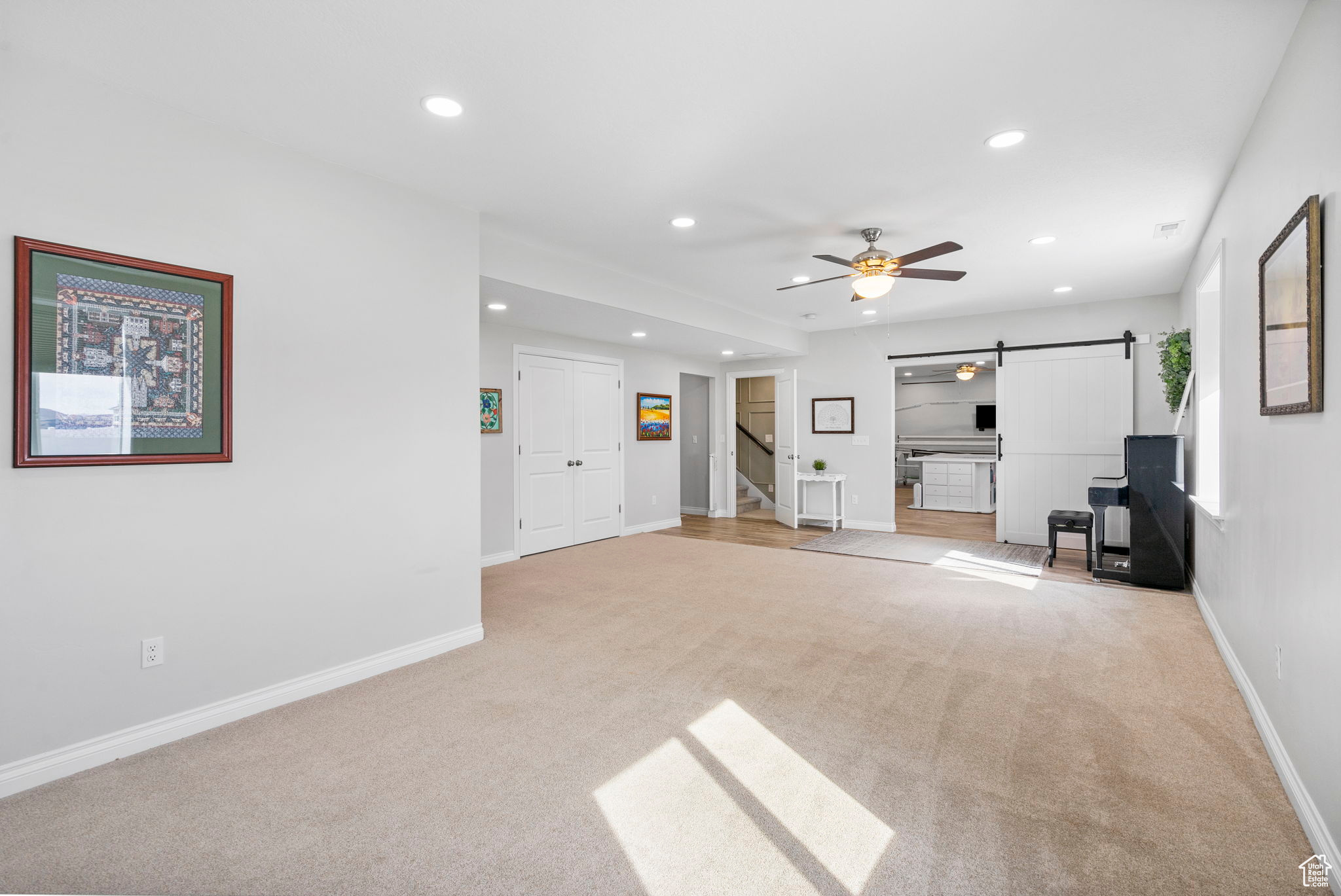 Unfurnished living room featuring recessed lighting, a barn door, baseboards, and light colored carpet