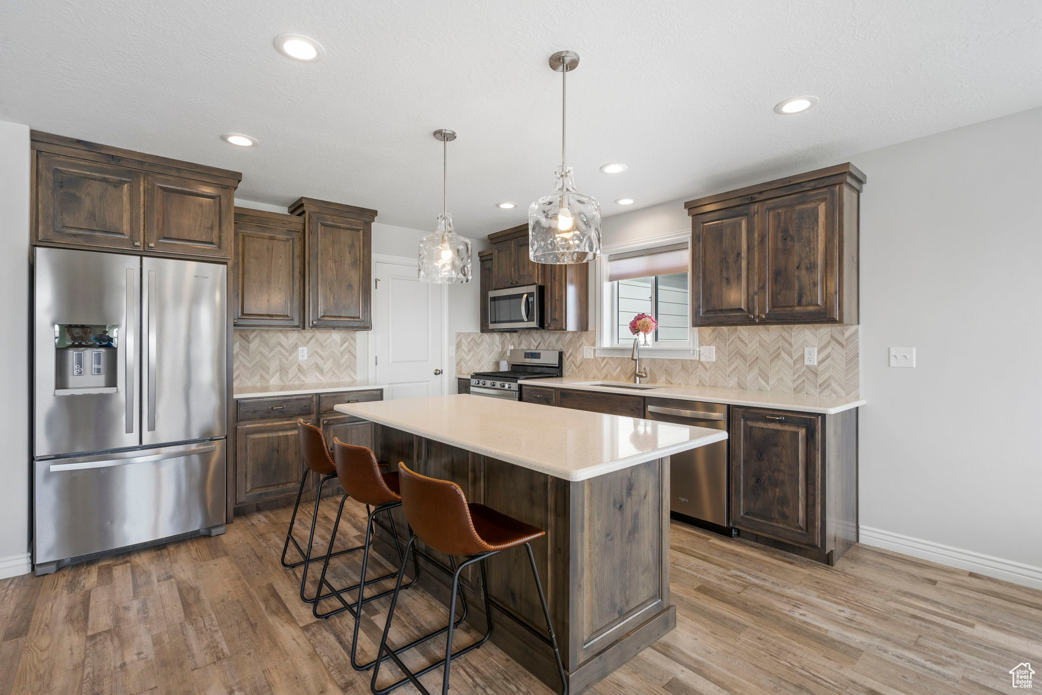 Kitchen with light wood finished floors, a sink, stainless steel appliances, dark brown cabinetry, and light countertops