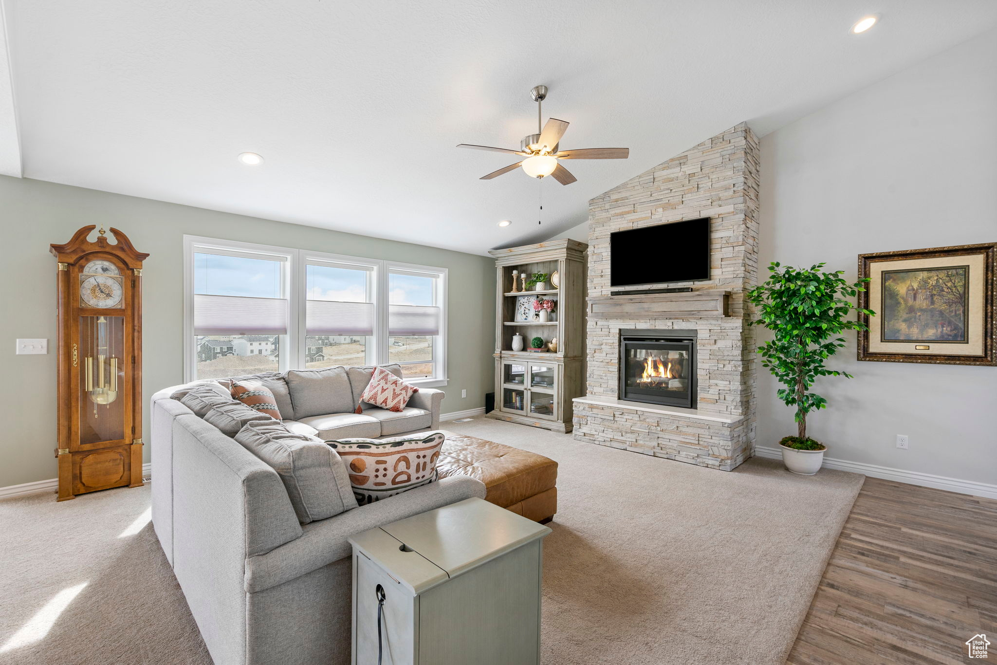 Living room featuring baseboards, lofted ceiling, a stone fireplace, and ceiling fan
