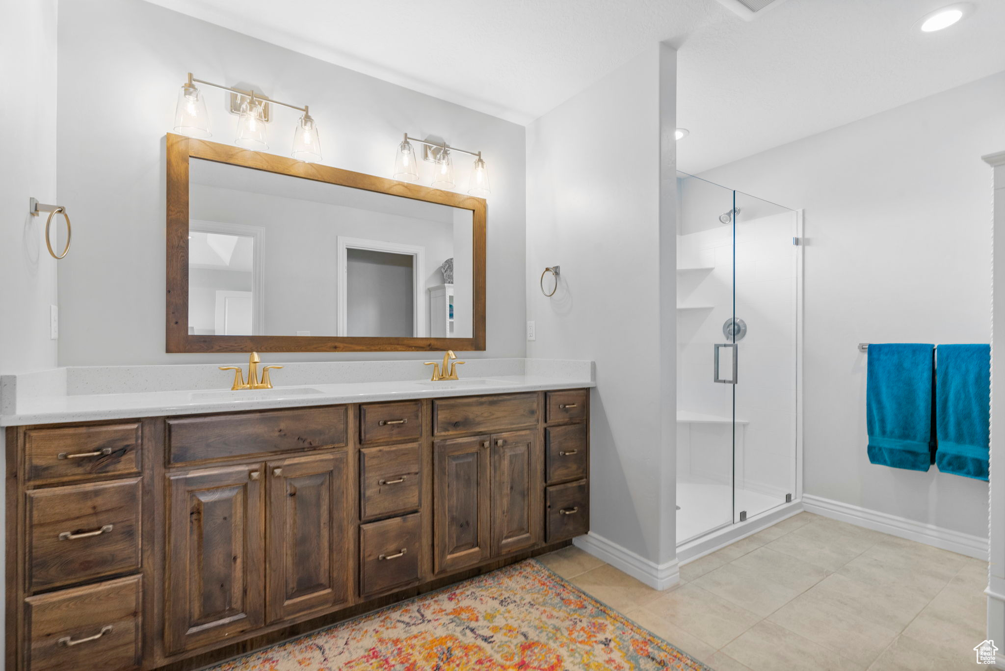 Full bath with a sink, a stall shower, double vanity, and tile patterned flooring