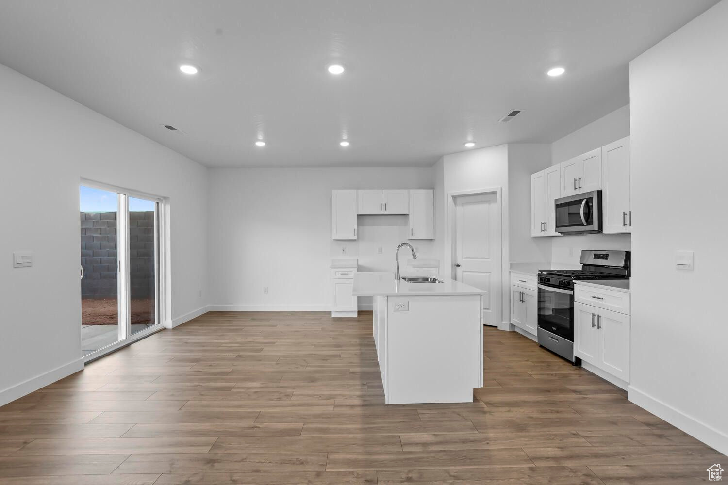 Kitchen featuring a sink, stainless steel appliances, a center island with sink, and light wood-style flooring