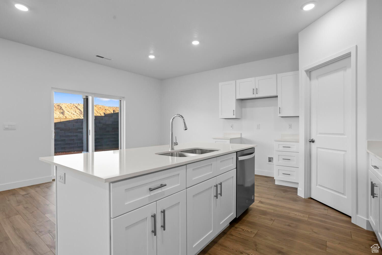 Kitchen featuring stainless steel dishwasher, wood finished floors, a center island with sink, and a sink