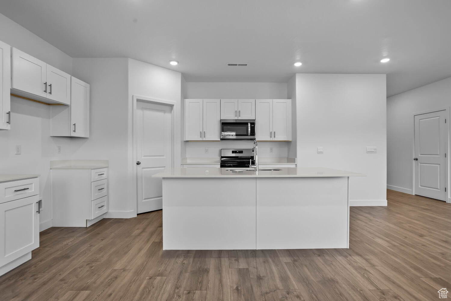 Kitchen featuring light countertops, white cabinets, wood finished floors, and stainless steel appliances