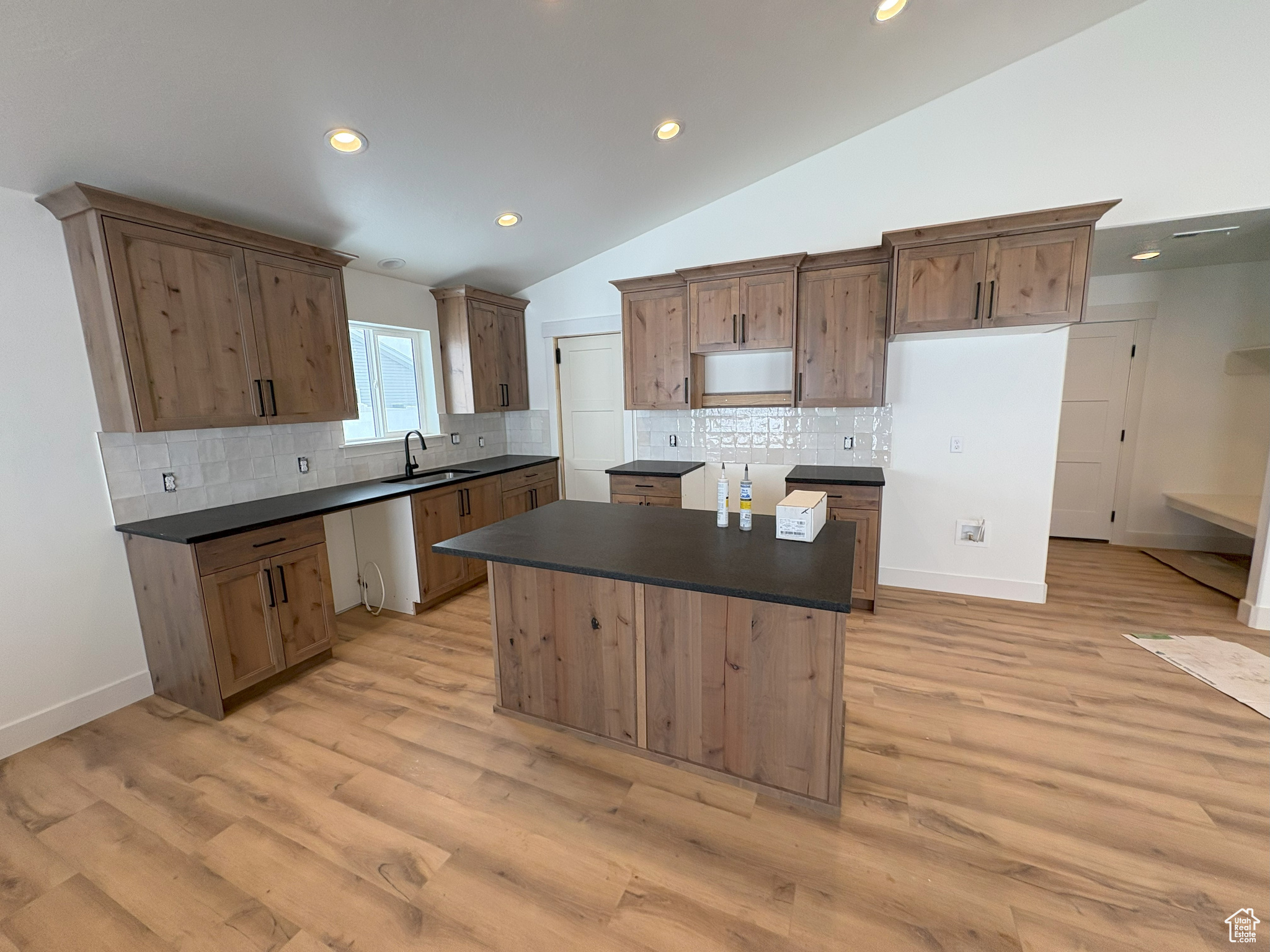 Kitchen with a sink, light wood-type flooring, a kitchen island, and dark countertops