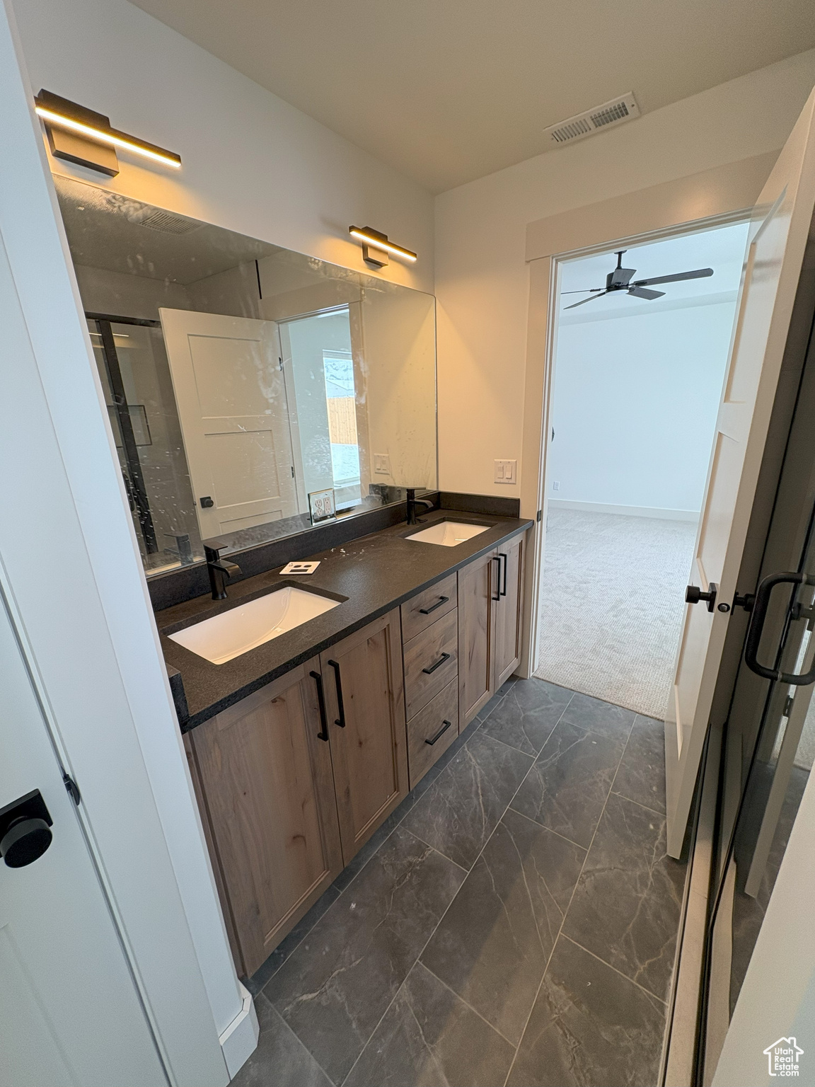 Full bath with a shower with door, visible vents, double vanity, marble finish floor, and a sink