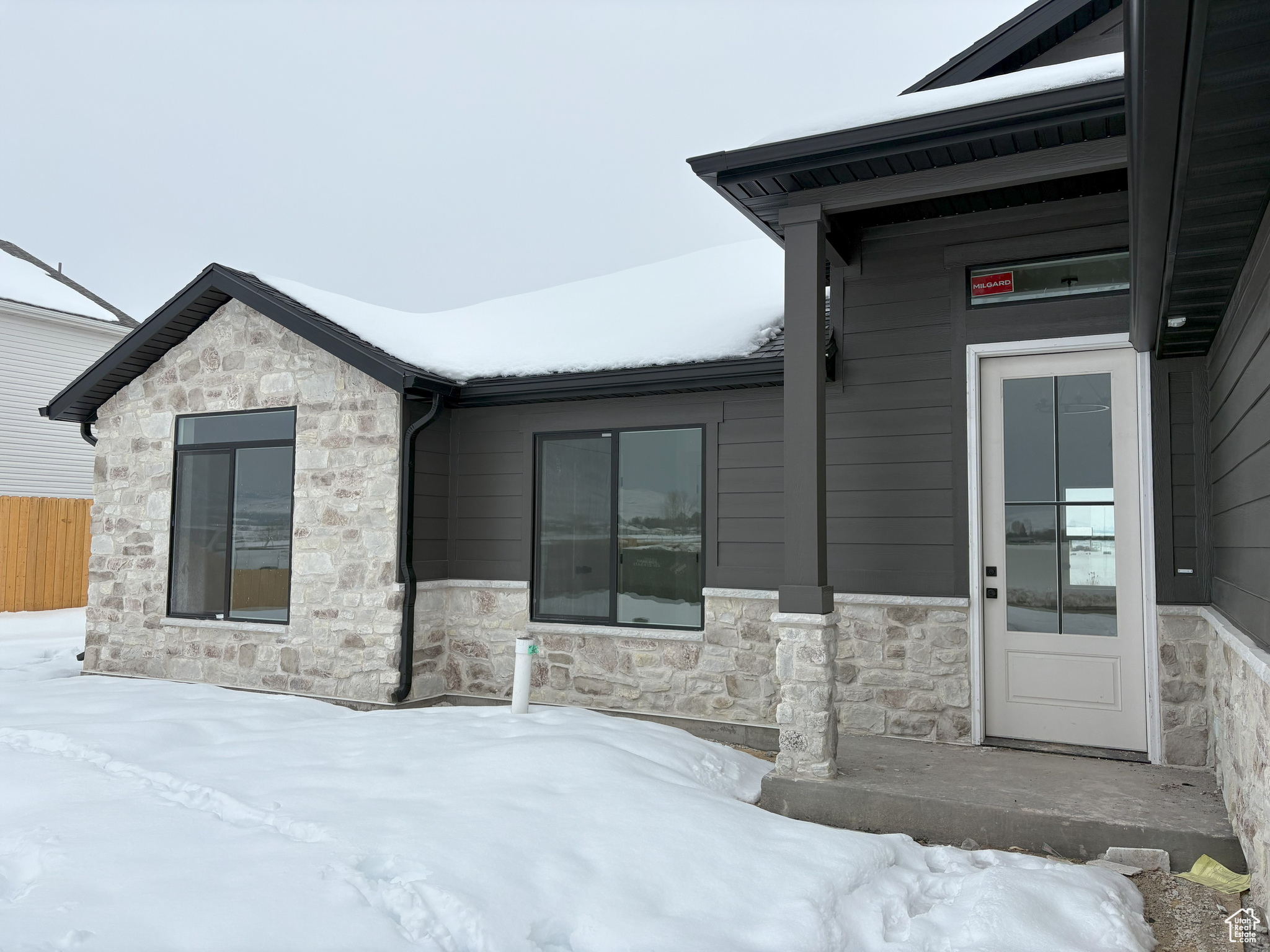 Snow covered property entrance with stone siding and fence