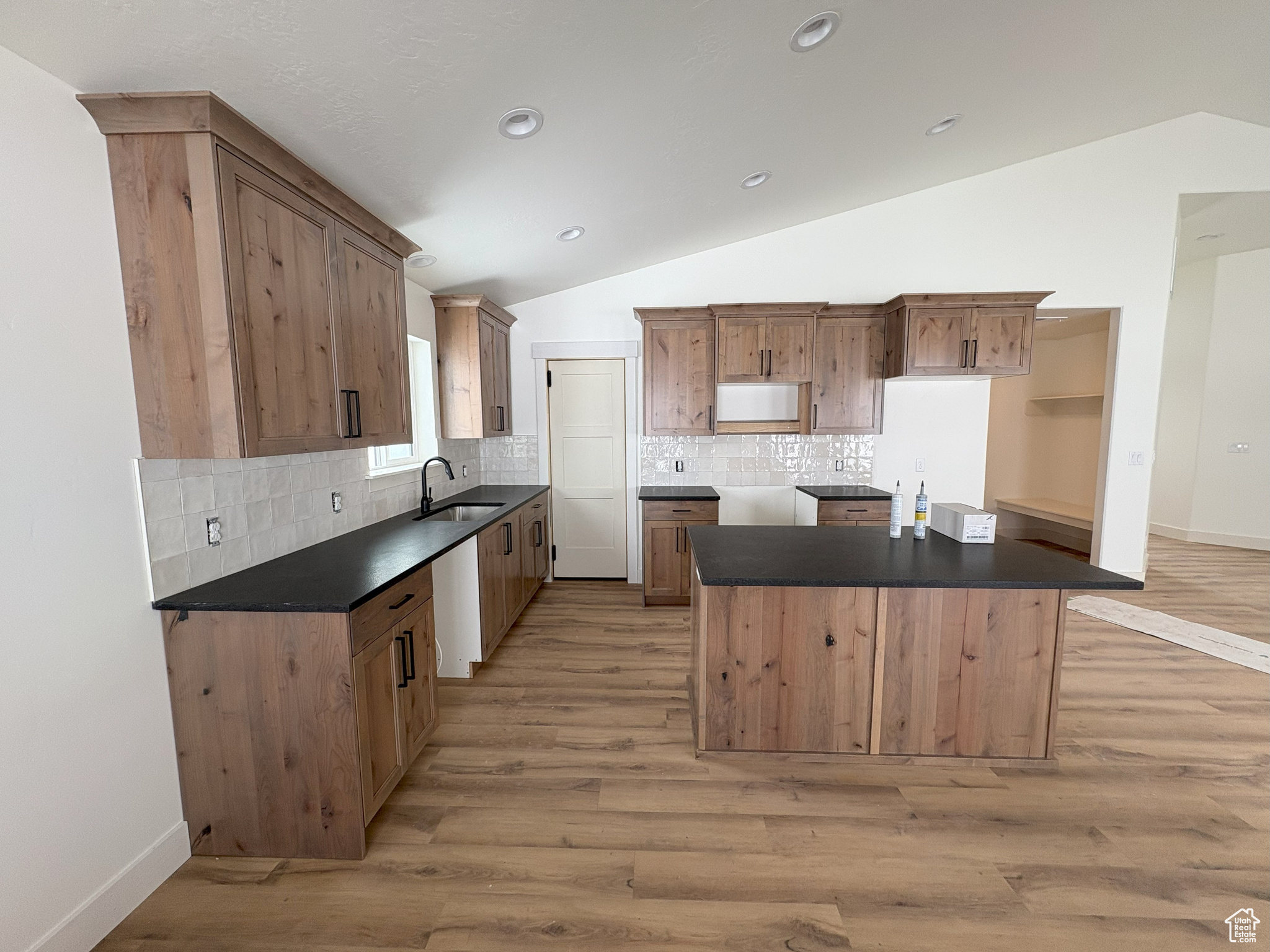 Kitchen with dark countertops, a center island, lofted ceiling, and a sink