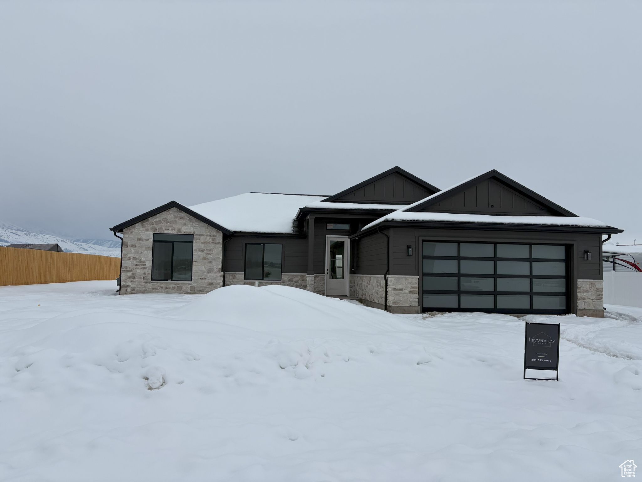 View of front of house with a garage, stone siding, board and batten siding, and fence