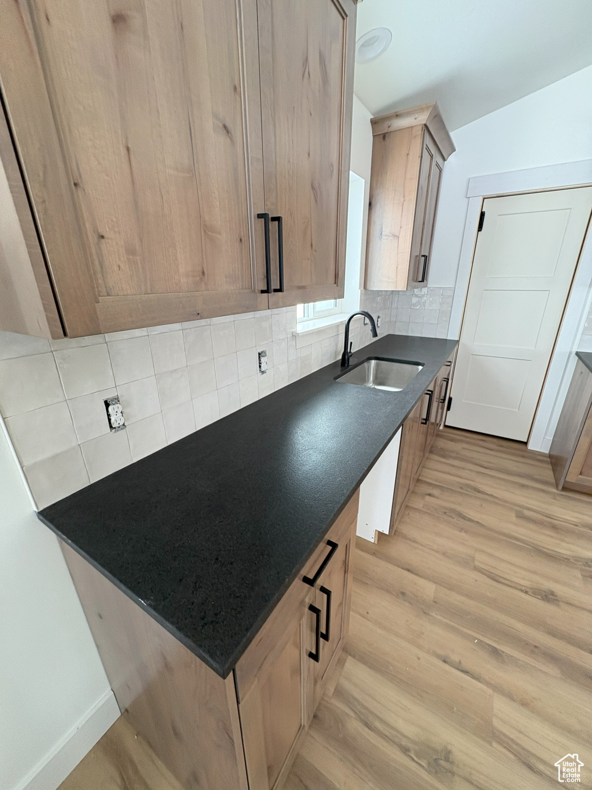 Kitchen with a sink, tasteful backsplash, light wood-style flooring, and dark stone countertops