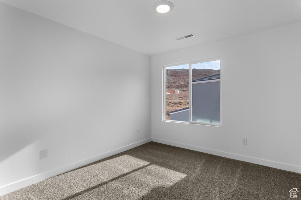 Empty room featuring visible vents, baseboards, and dark colored carpet