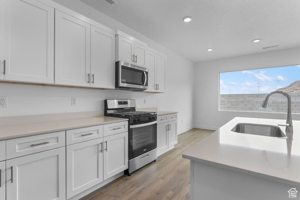 Kitchen featuring light wood finished floors, a sink, stainless steel appliances, light countertops, and white cabinetry