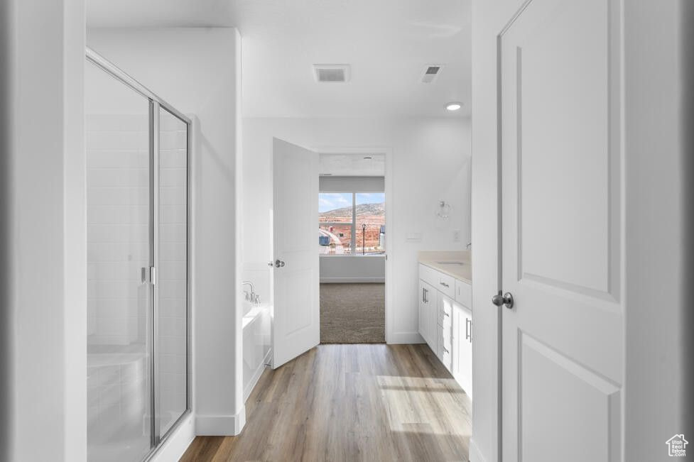 Bathroom featuring a shower stall, a garden tub, wood finished floors, and baseboards