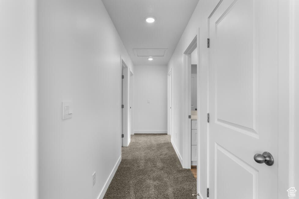 Hall with attic access, baseboards, and dark colored carpet