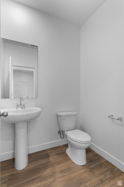 Bathroom with toilet, wood finished floors, baseboards, and a sink