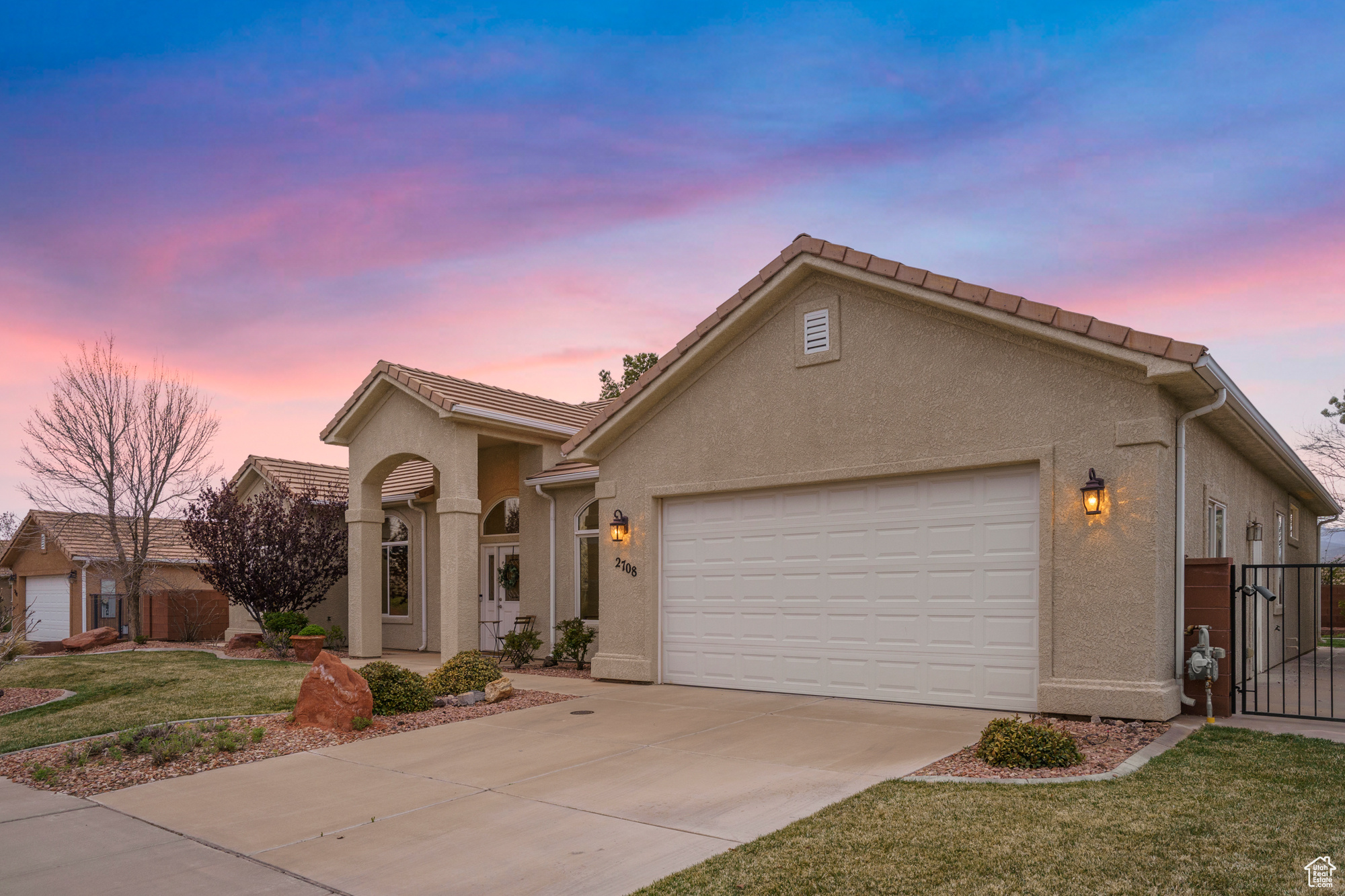 Mediterranean / spanish house with a front yard, stucco siding, driveway, an attached garage, and a gate