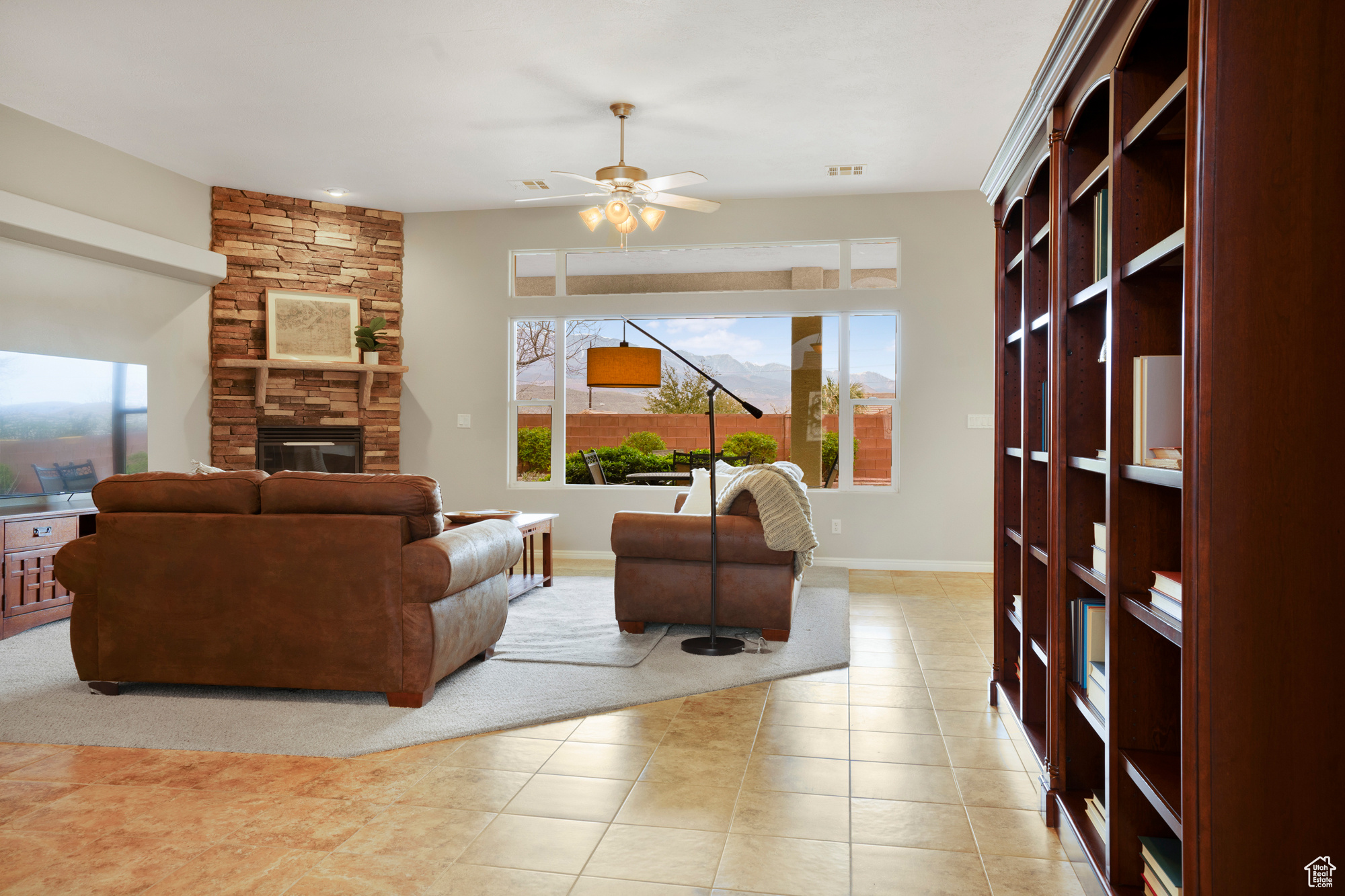 Living area featuring a wealth of natural light, a stone fireplace, ceiling fan, and light tile patterned floors