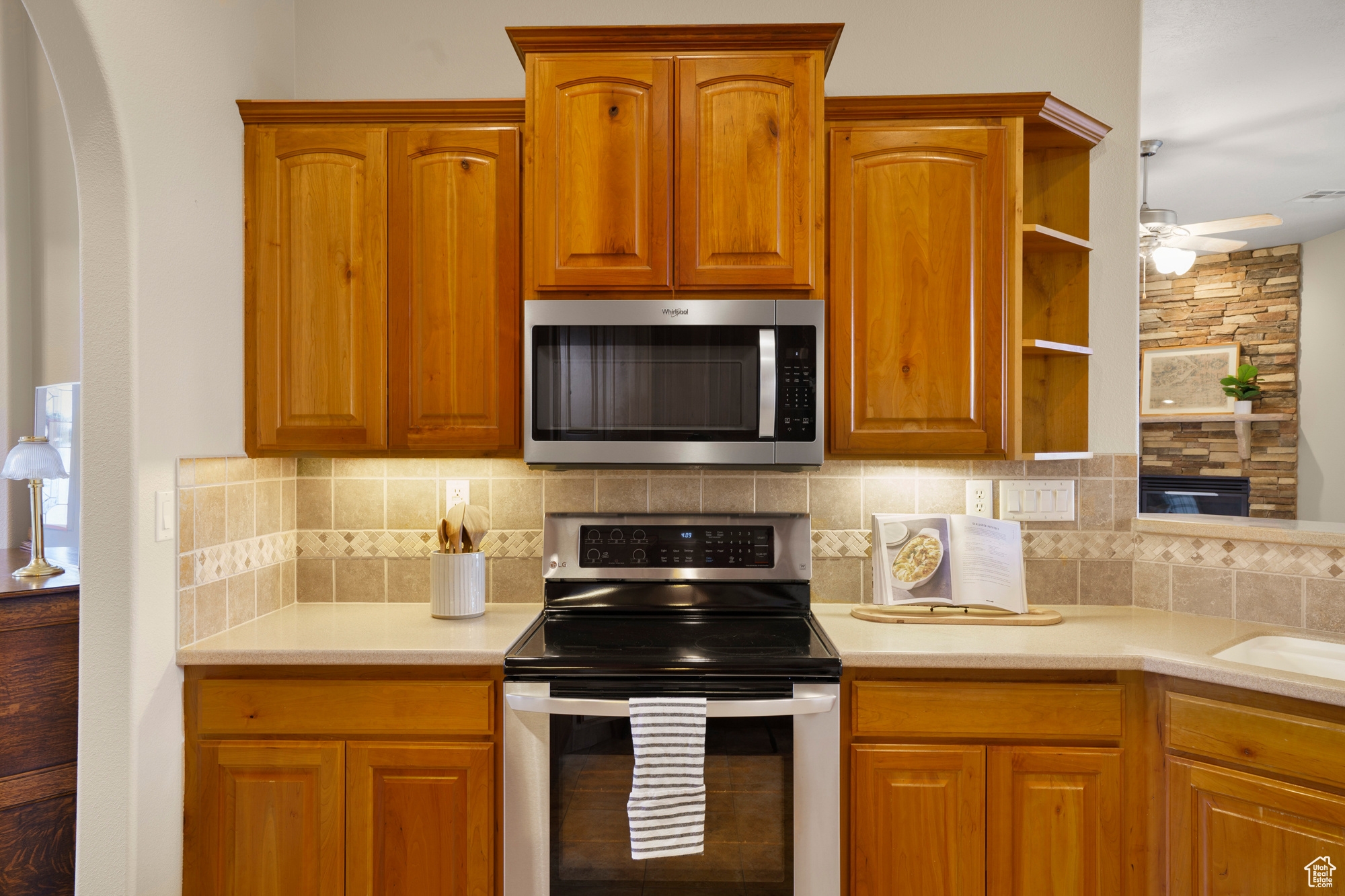 Kitchen featuring open shelves, ceiling fan, light countertops, appliances with stainless steel finishes, and backsplash