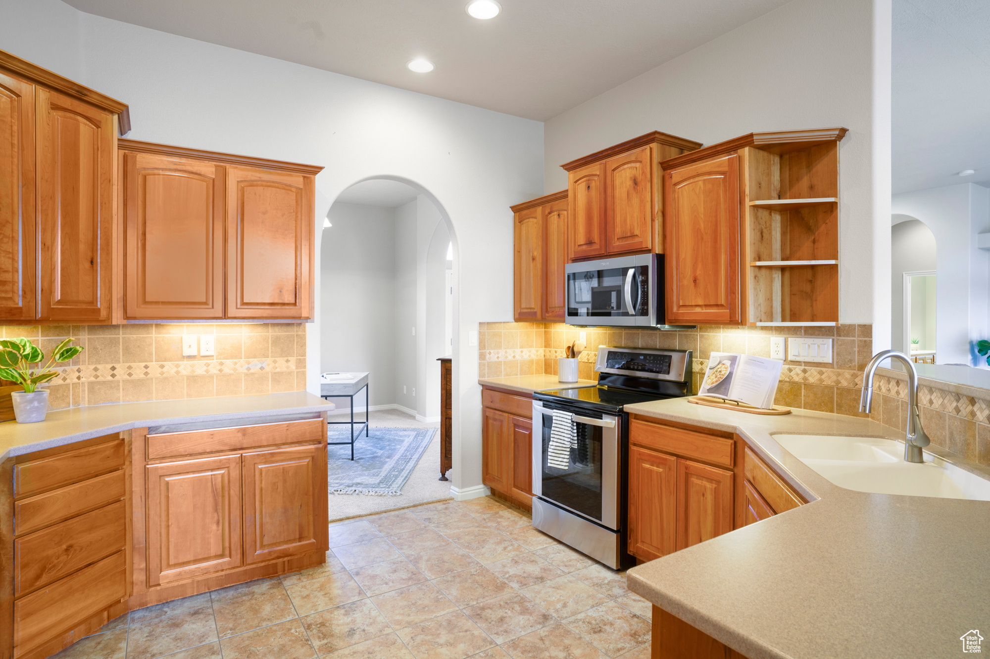 Kitchen with a sink, open shelves, stainless steel appliances, arched walkways, and light countertops
