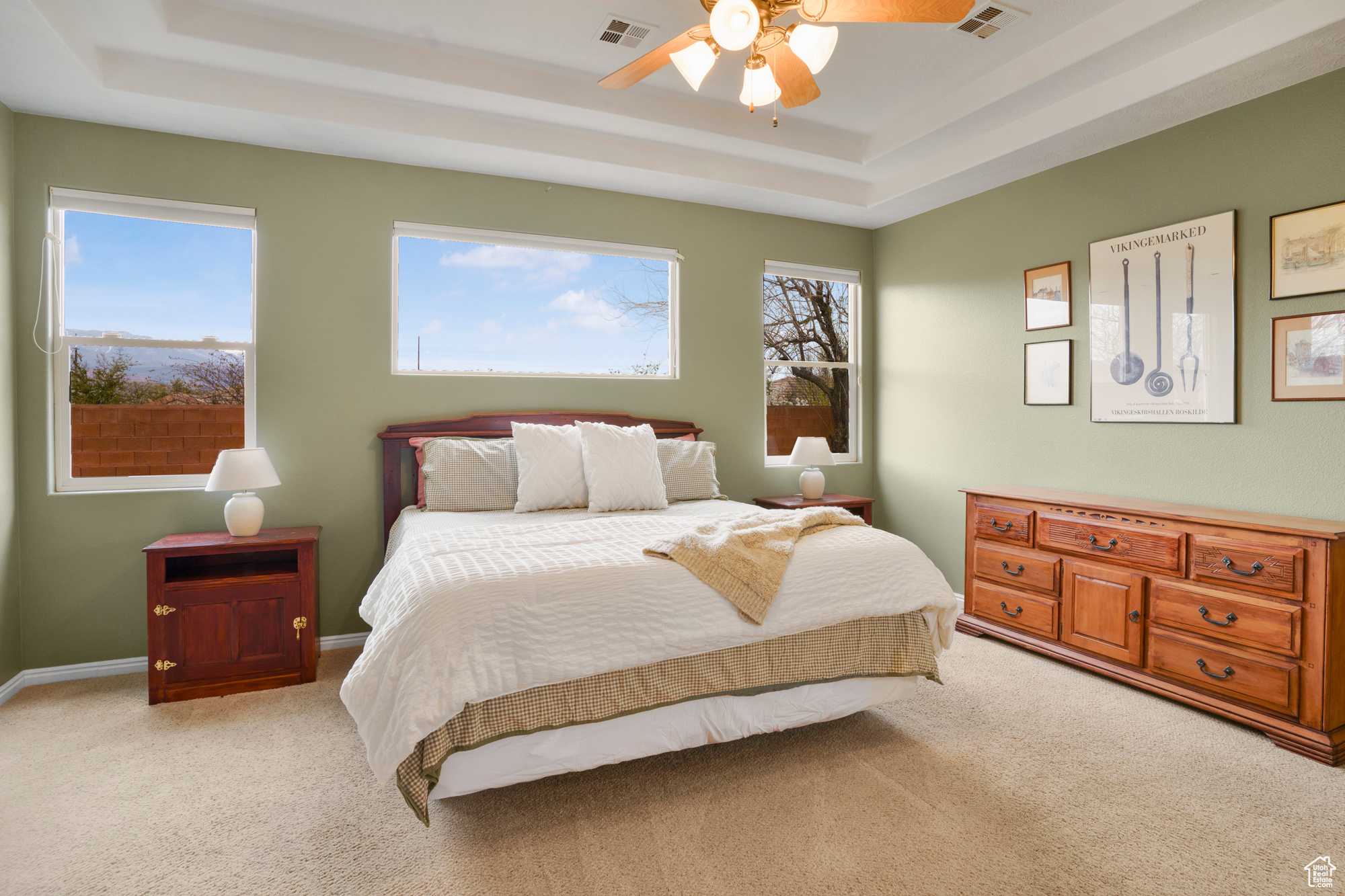 Bedroom with a tray ceiling, multiple windows, light colored carpet, and visible vents