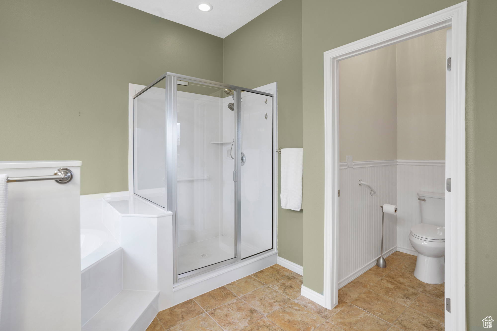 Bathroom with a wainscoted wall, toilet, a stall shower, and a bath