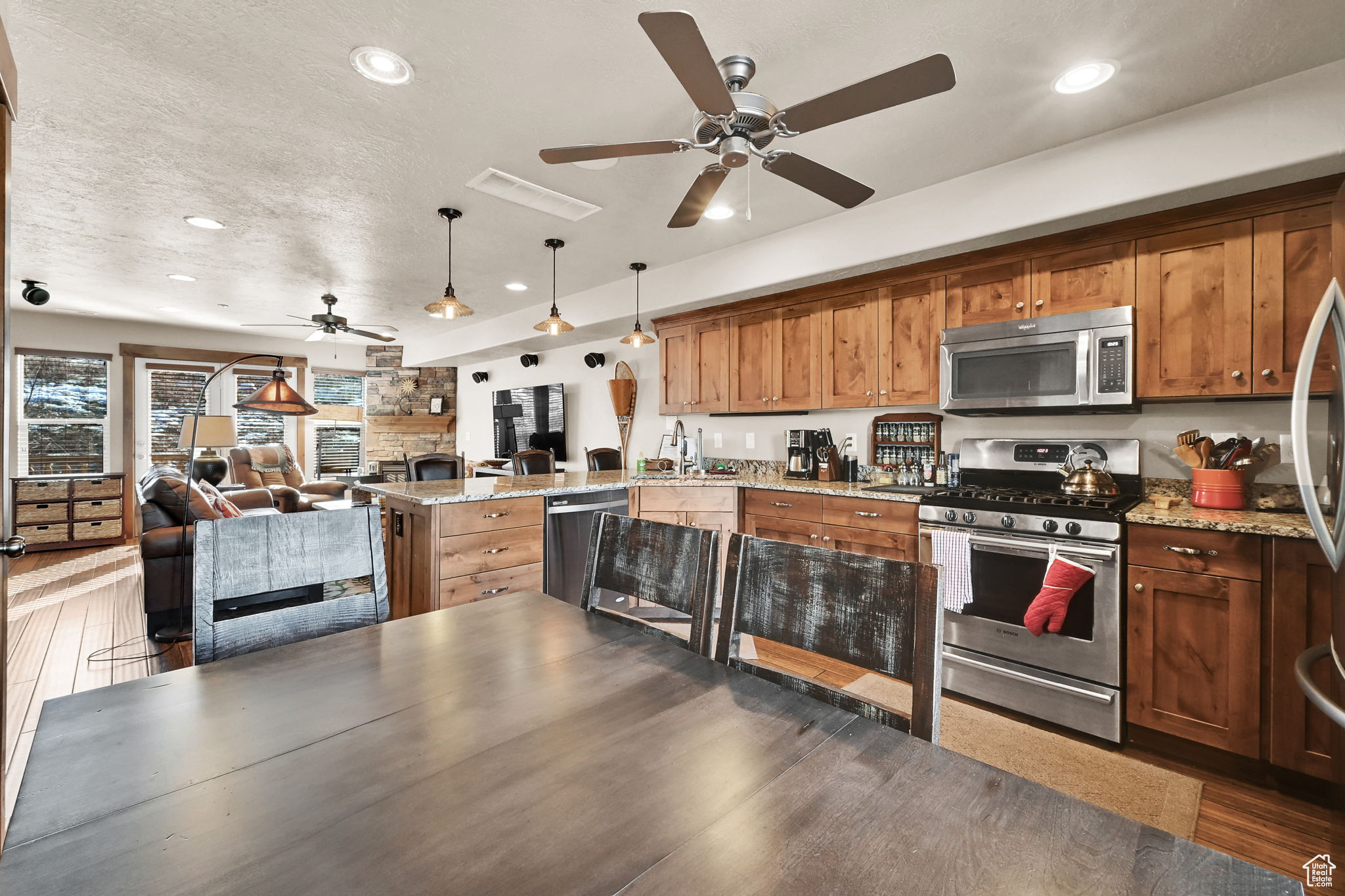 Kitchen with open floor plan, a peninsula, wood finished floors, brown cabinetry, and stainless steel appliances