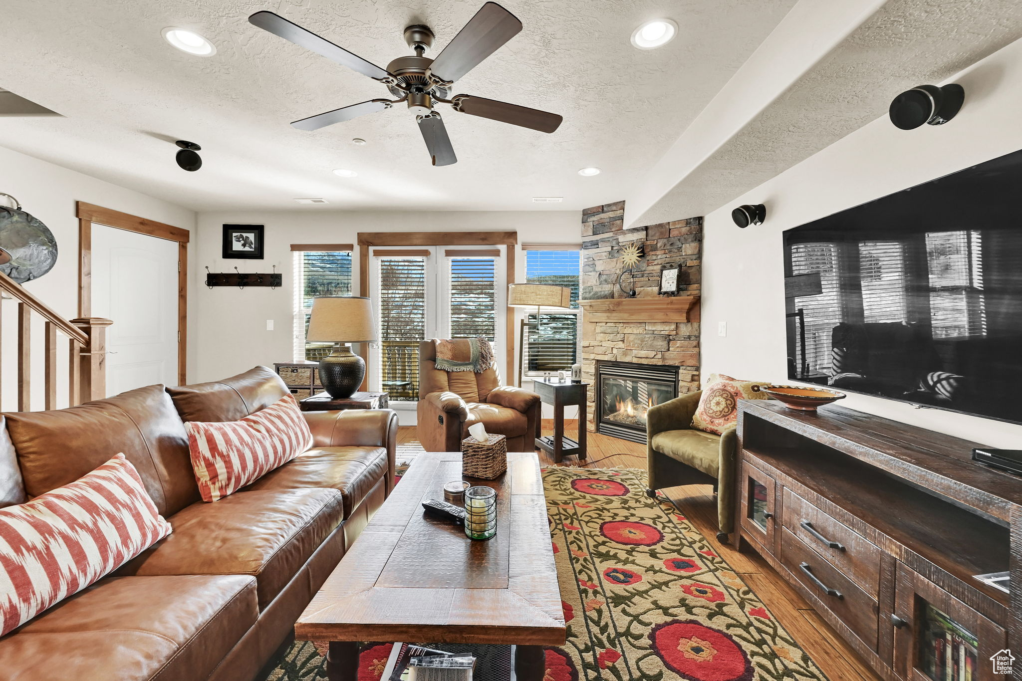 Living room with a stone fireplace, recessed lighting, a textured ceiling, and light wood-style floors