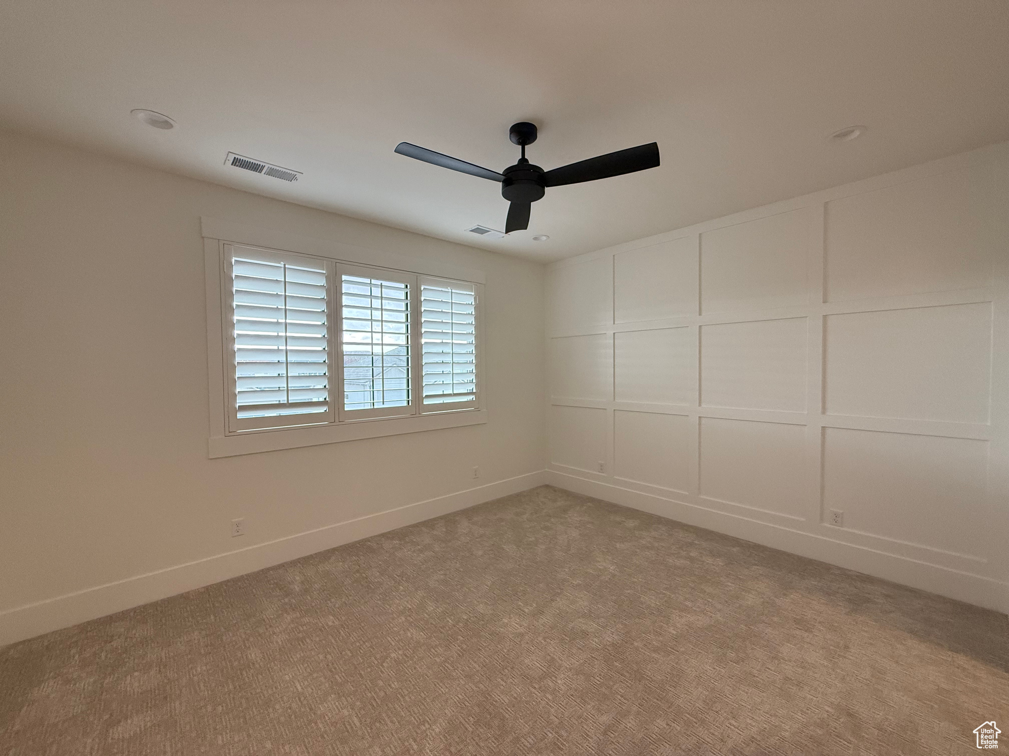 Unfurnished room with visible vents, light colored carpet, a ceiling fan, and a decorative wall