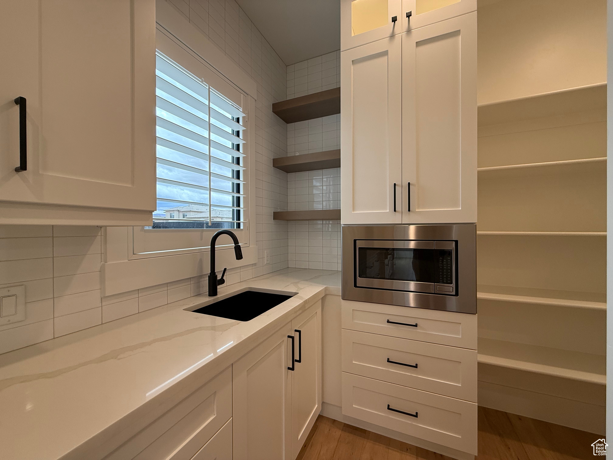 Kitchen with stainless steel microwave, open shelves, light stone counters, white cabinets, and a sink