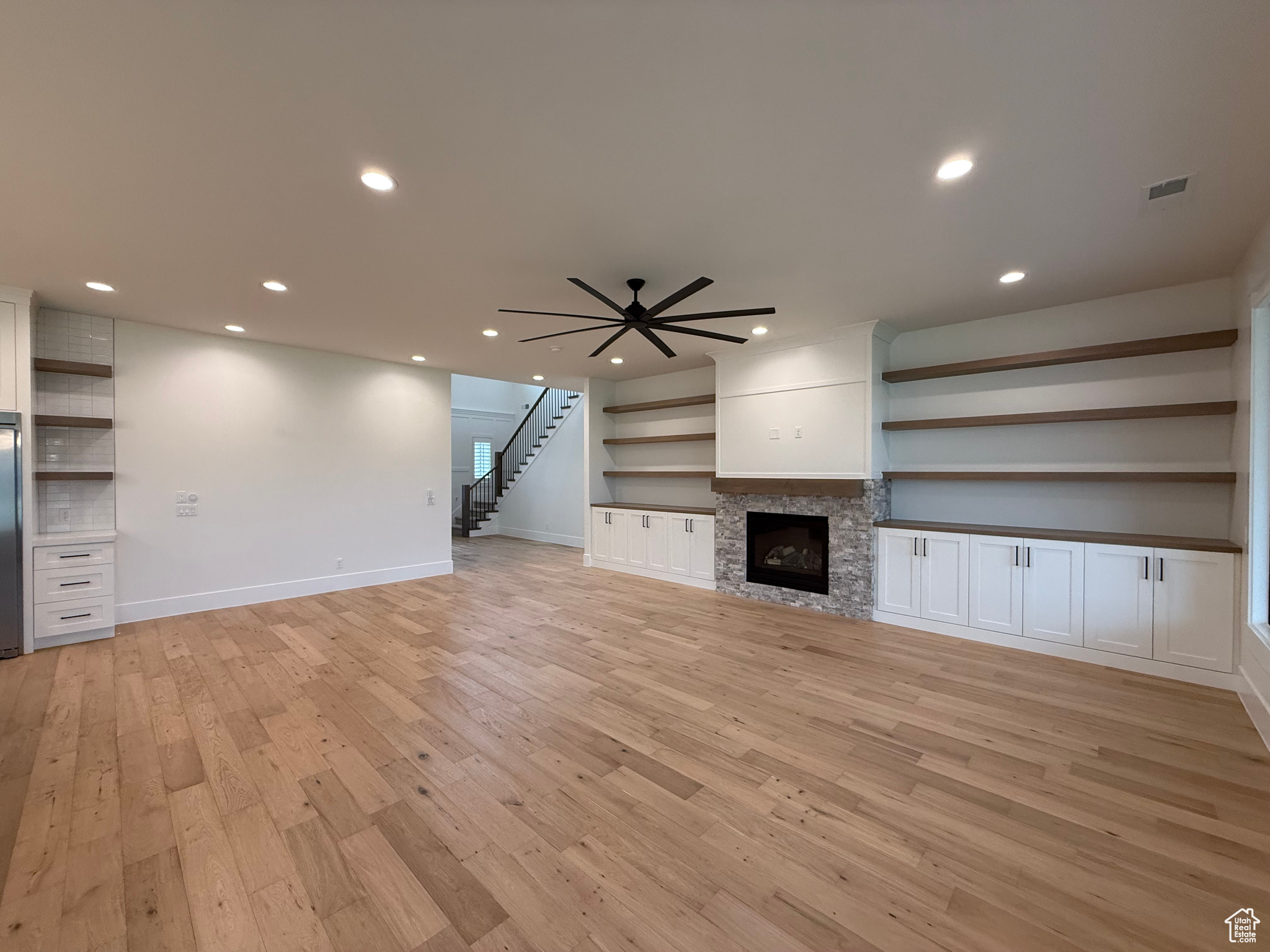 Unfurnished living room featuring stairway, recessed lighting, a fireplace, light wood-style floors, and a ceiling fan