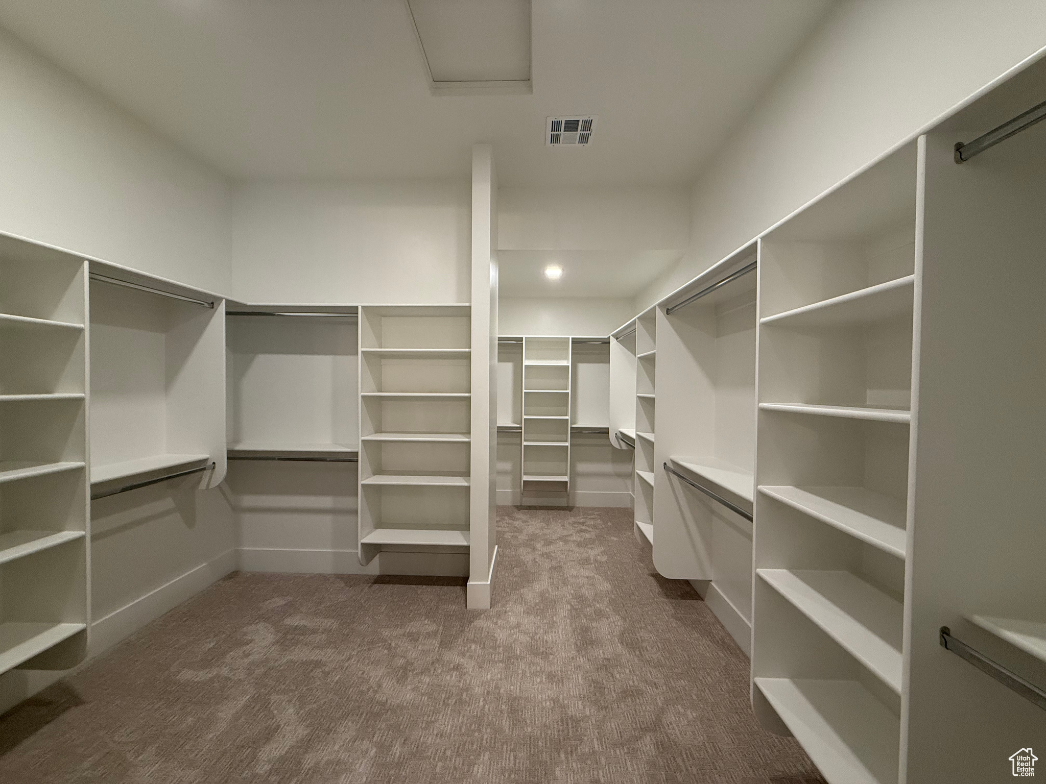 Spacious closet with visible vents, attic access, and dark carpet