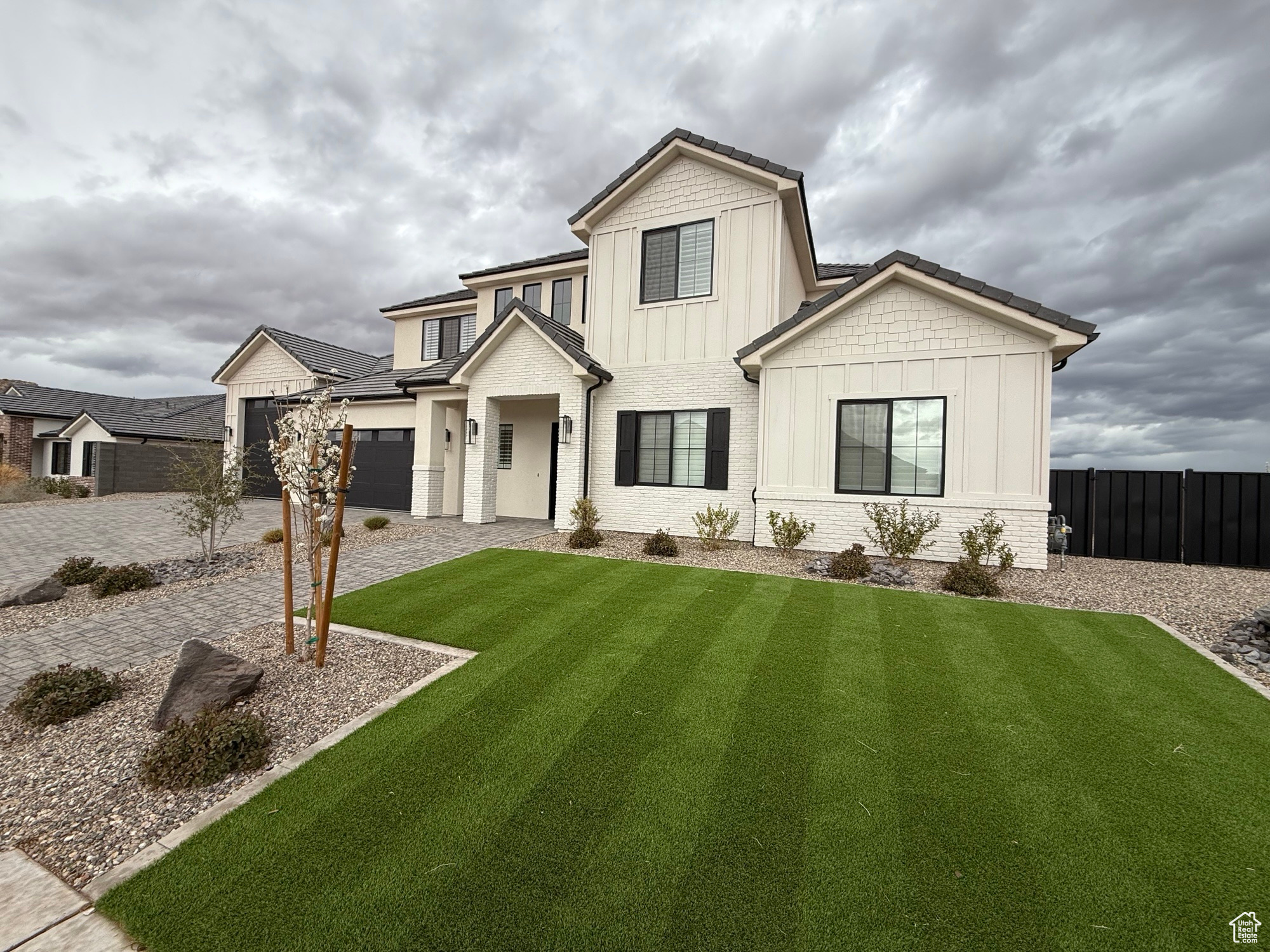 Modern inspired farmhouse featuring a front lawn, decorative driveway, fence, board and batten siding, and brick siding