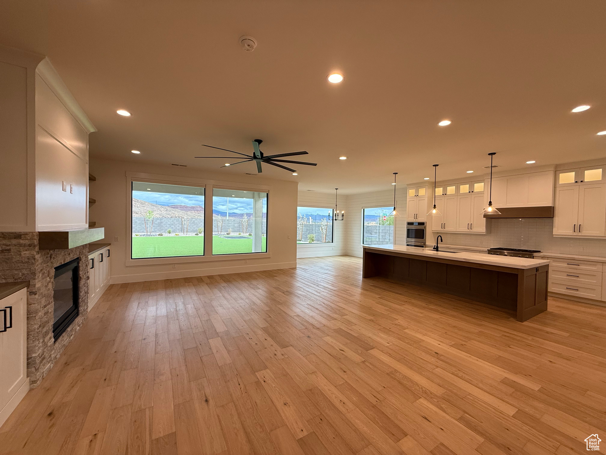 Interior space featuring under cabinet range hood, open floor plan, stainless steel oven, white cabinets, and a sink