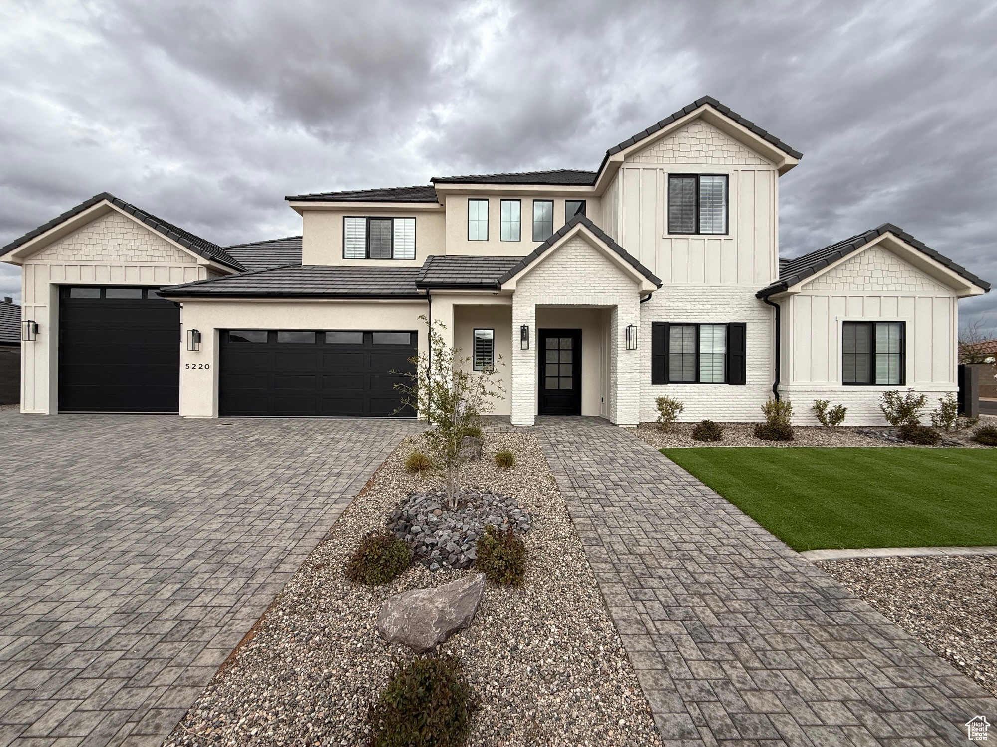 Modern inspired farmhouse with brick siding, board and batten siding, a front yard, decorative driveway, and a garage