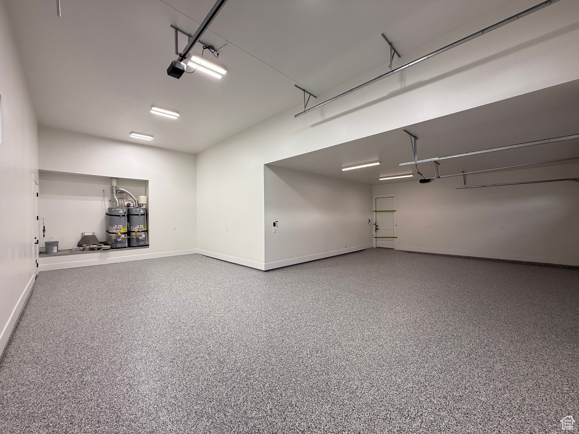 Garage with strapped water heater, a garage door opener, and baseboards