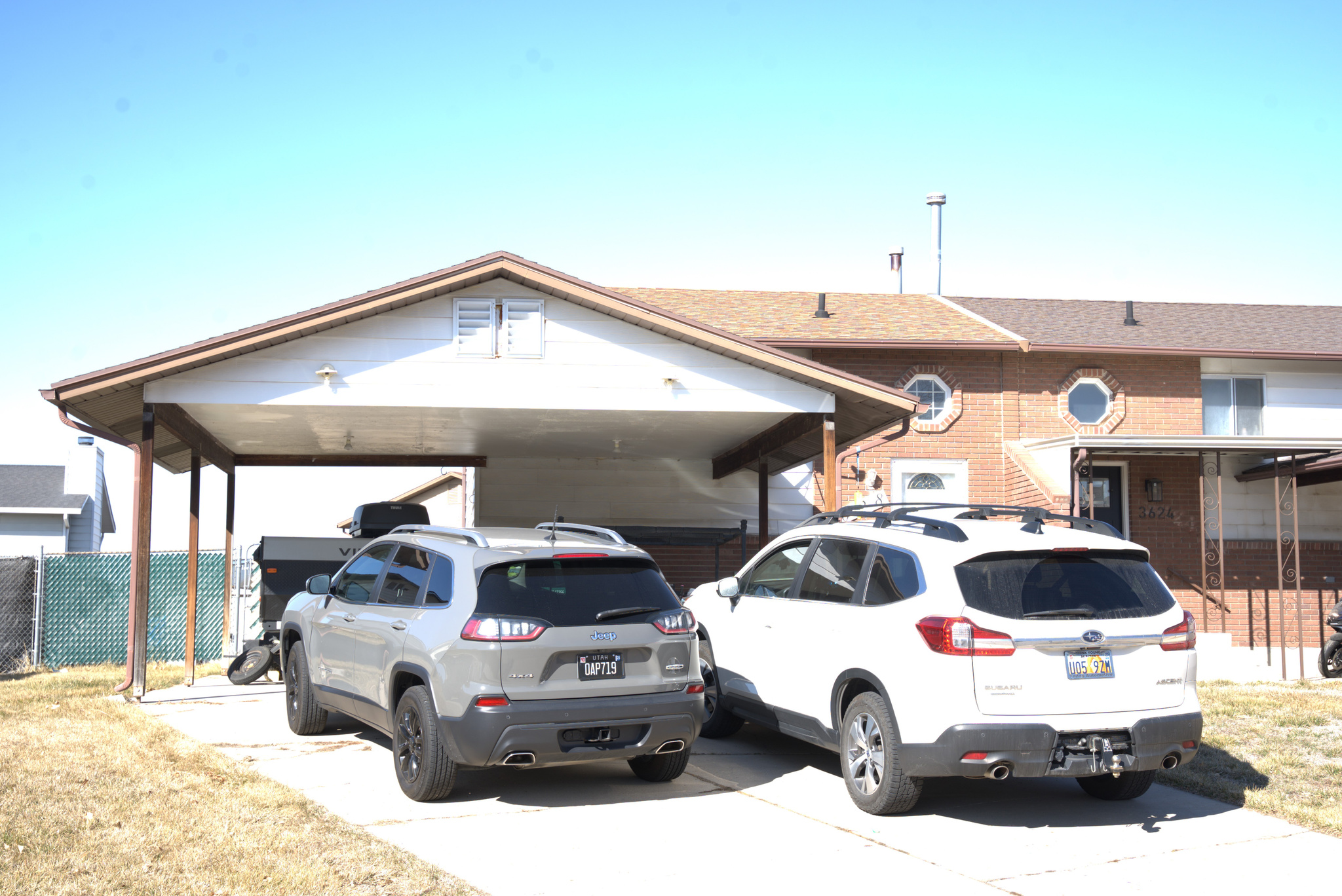 View of front of property with a carport, concrete driveway, brick siding, and fence