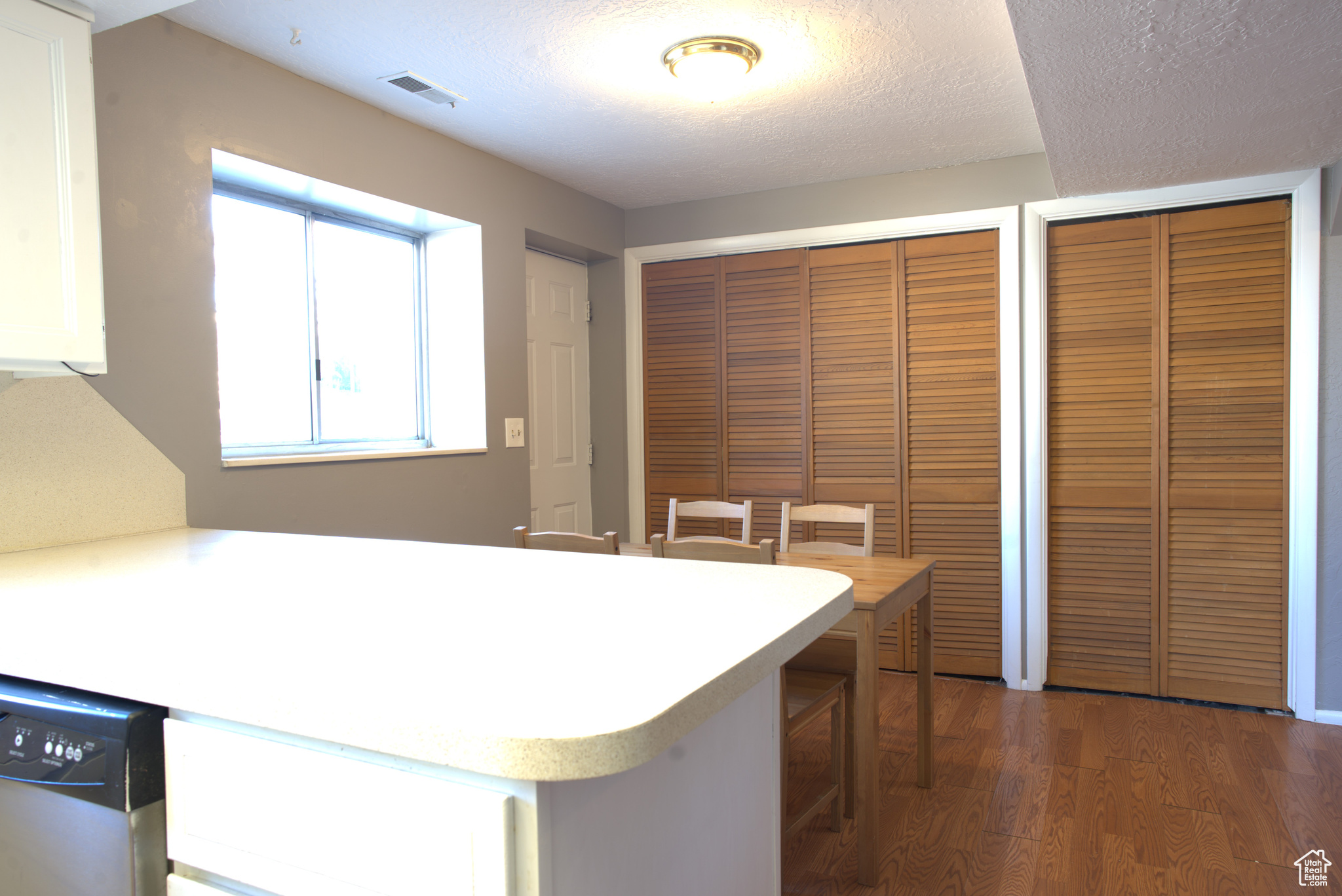 Kitchen featuring visible vents, light countertops, wood finished floors, a textured ceiling, and stainless steel dishwasher