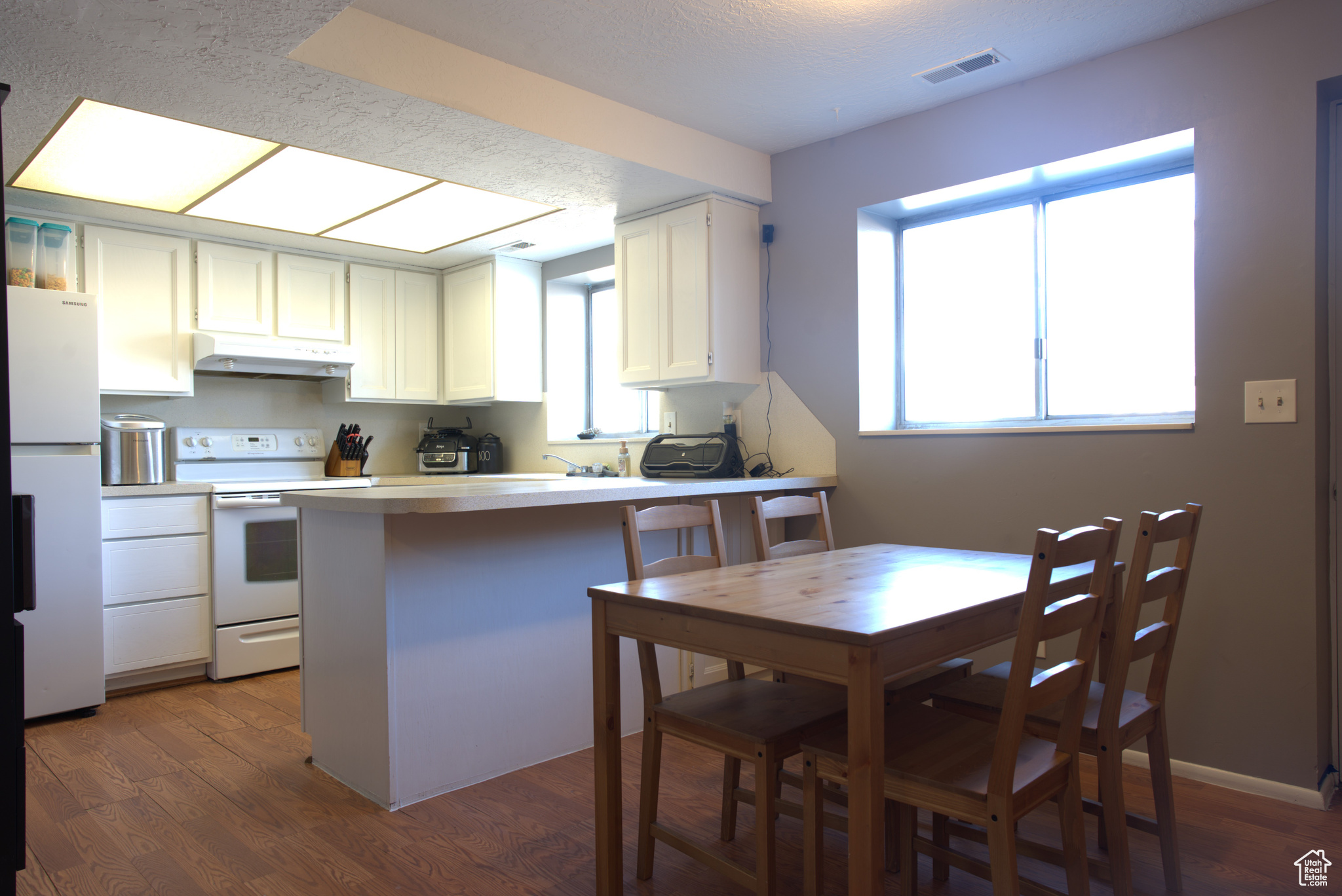 Kitchen with under cabinet range hood, visible vents, white appliances, and a healthy amount of sunlight