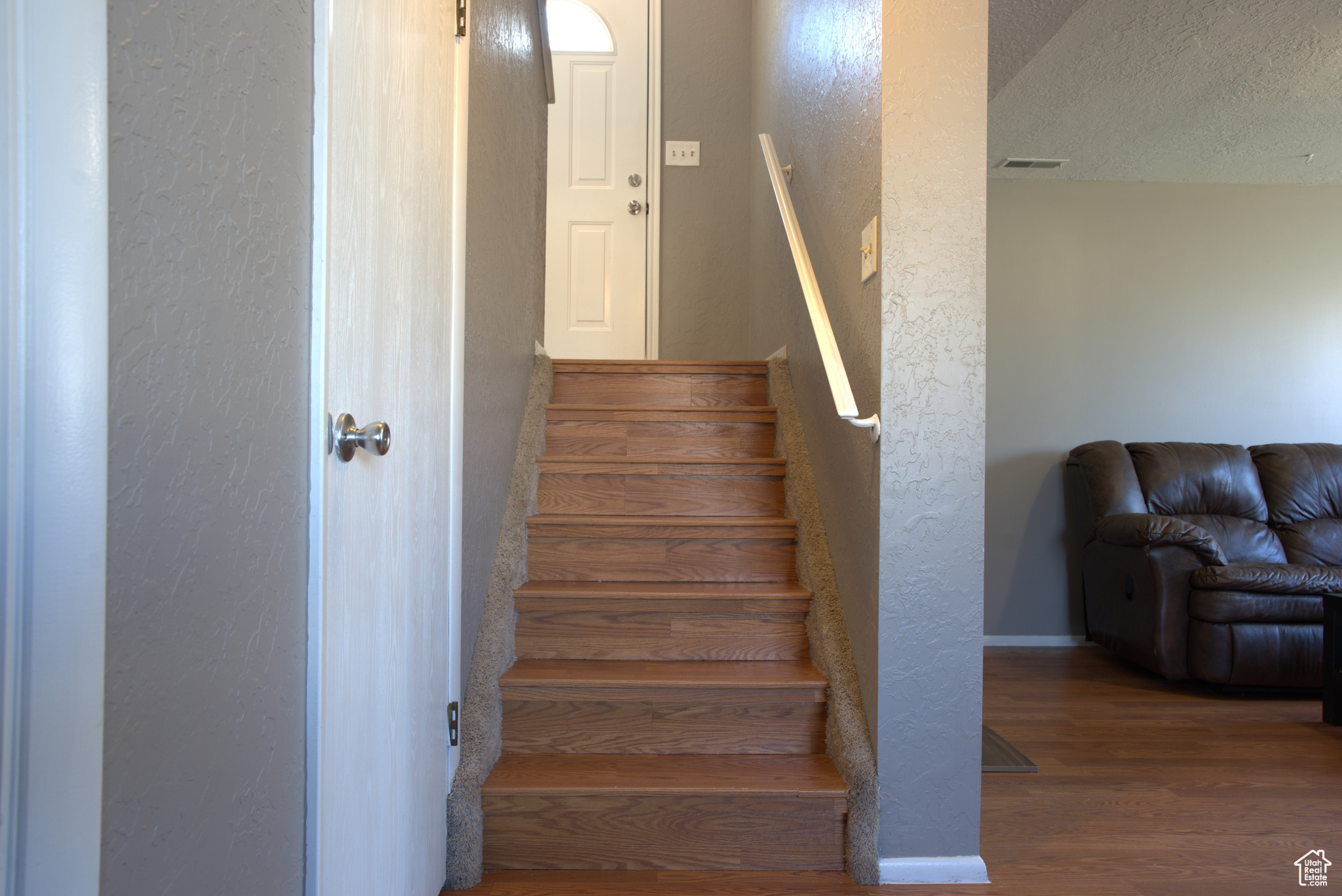 Stairs featuring visible vents, a textured ceiling, wood finished floors, and a textured wall