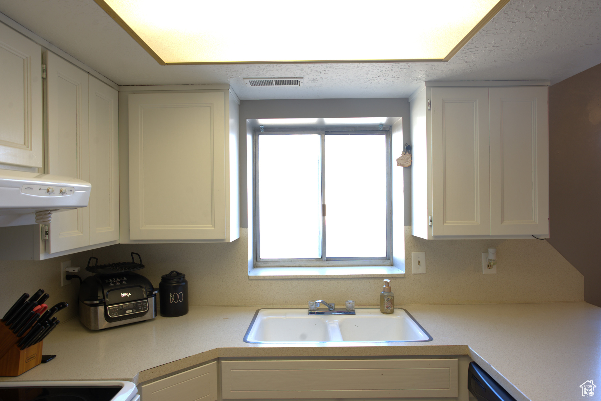 Kitchen with a sink, visible vents, white cabinets, and light countertops