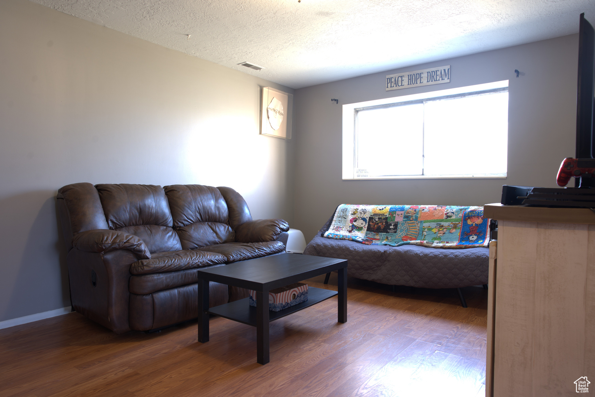 Living room featuring visible vents, a textured ceiling, baseboards, and wood finished floors