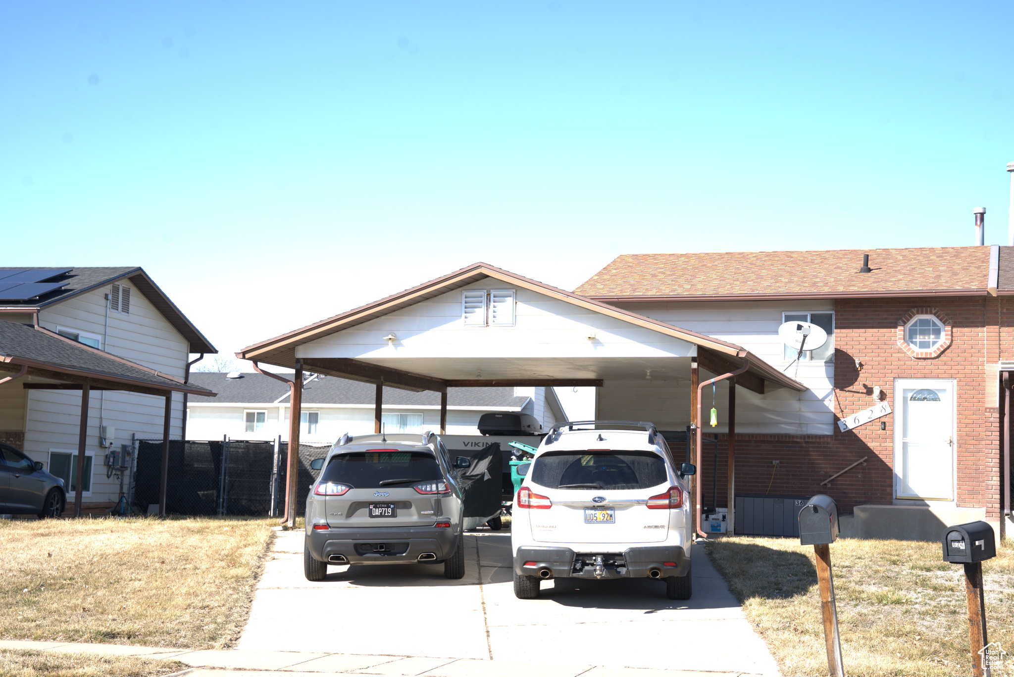 View of front of property with fence, concrete driveway, a shingled roof, an attached carport, and brick siding