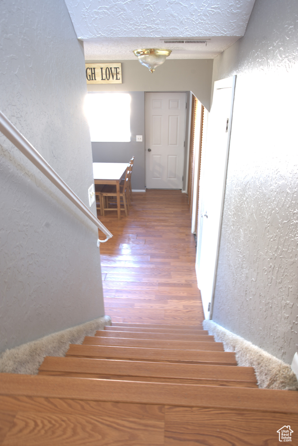 Stairs with wood finished floors, visible vents, arched walkways, a textured ceiling, and a textured wall