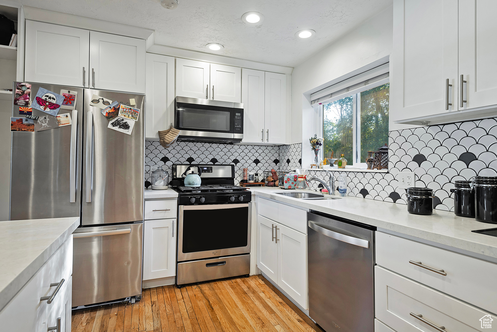 Kitchen featuring light wood finished floors, a sink, stainless steel appliances, light countertops, and white cabinetry