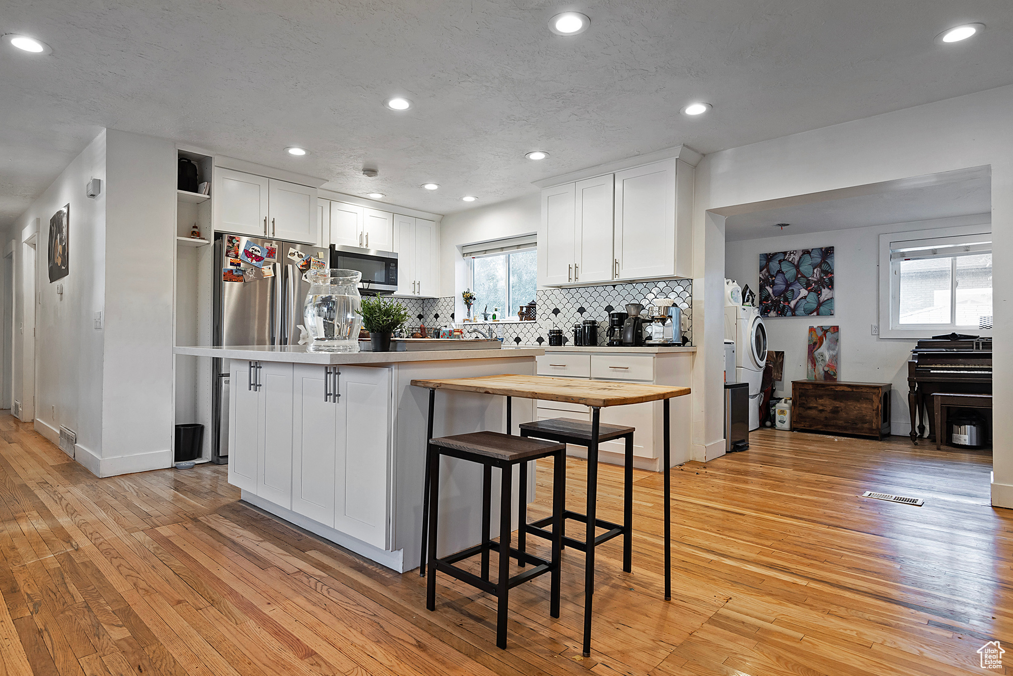 Kitchen with recessed lighting, decorative backsplash, white cabinets, light wood-style floors, and appliances with stainless steel finishes